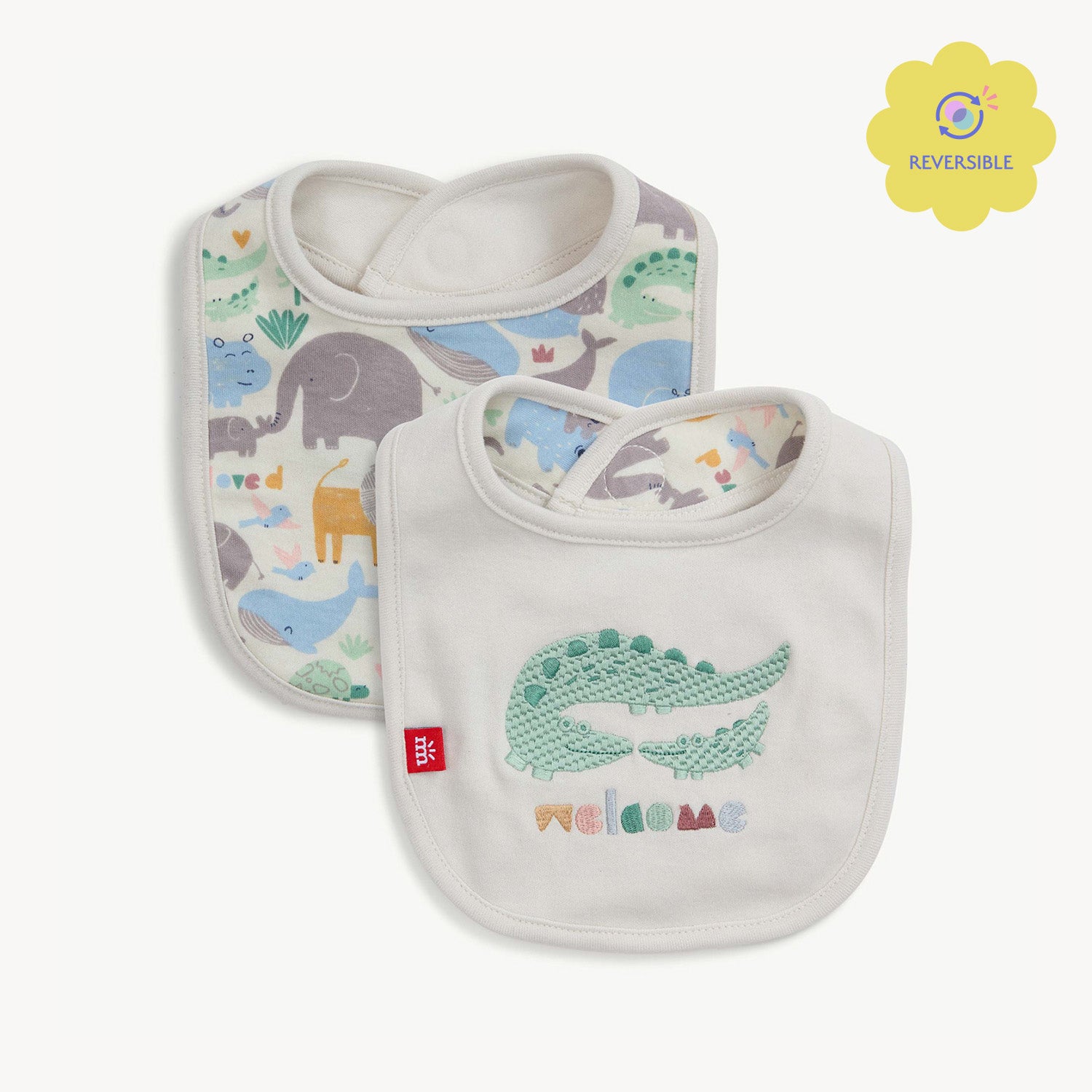 A cream-colored reversible infant bib with a green crocodile and "welcome" embroidery hanging from a clothesline  by Magnetic Me.
