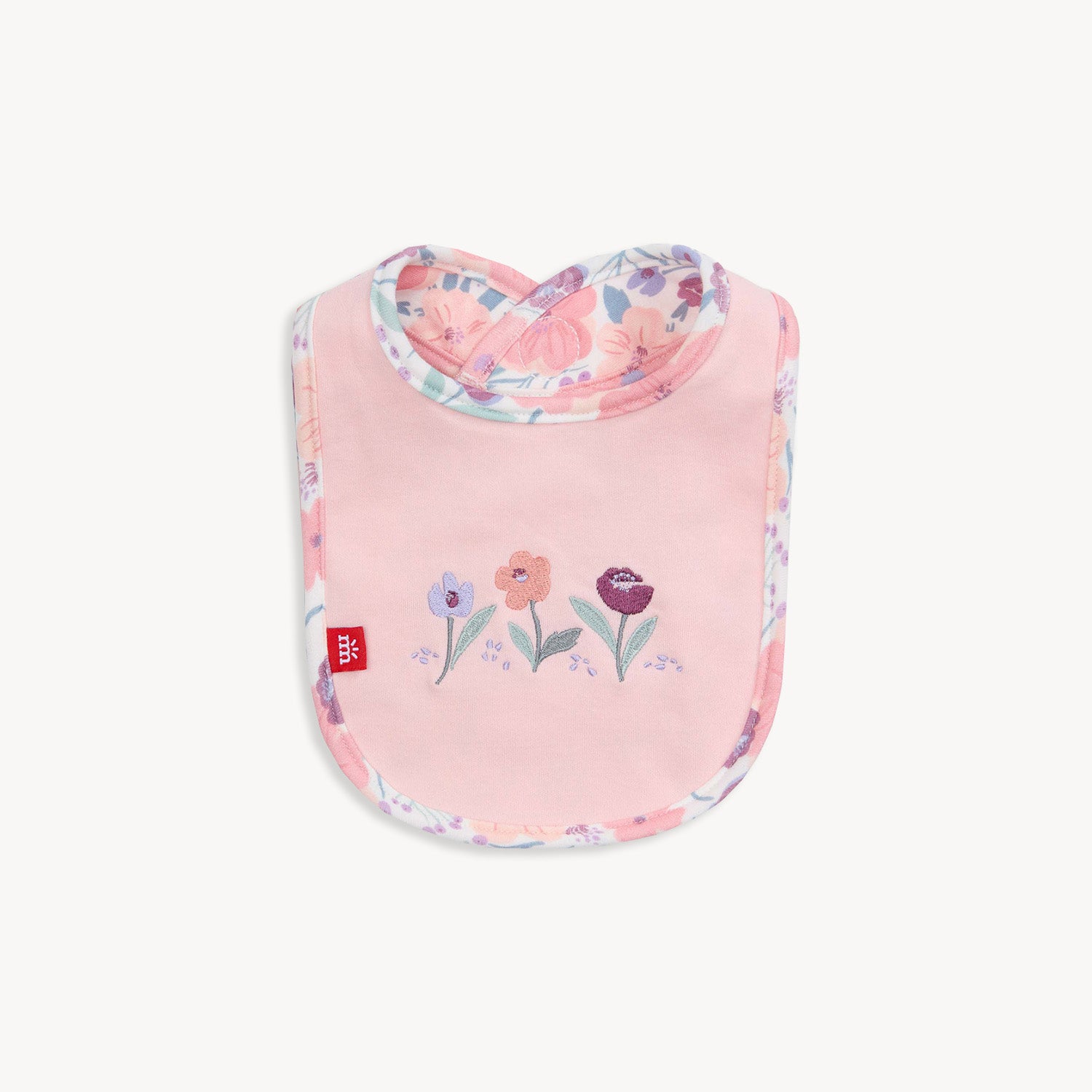A reversible infant bib featuring a solid pink side with floral embroidery and a white reverse side with an all-over floral print by Magnetic Me.