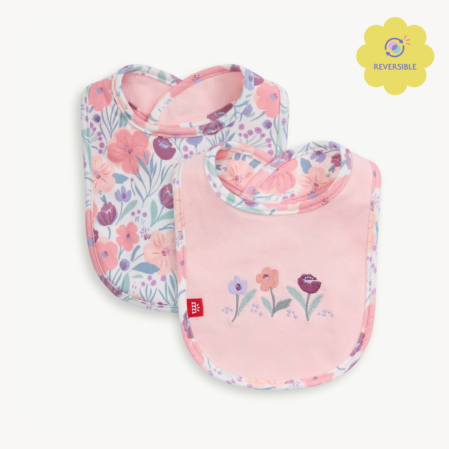 A reversible infant bib featuring a solid pink side with floral embroidery and a white reverse side with an all-over floral print by Magnetic Me.