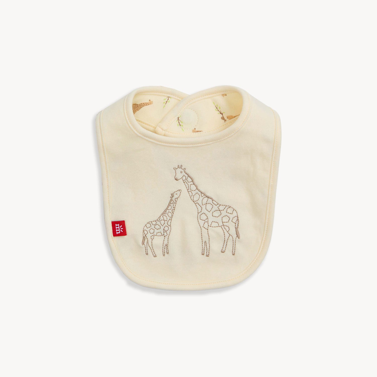 A cream-colored reversible bib featuring a large embroidered giraffe and baby giraffe on a solid background, with a repeat Jolie Giraffe print on the reverse side, by Magnetic Me.