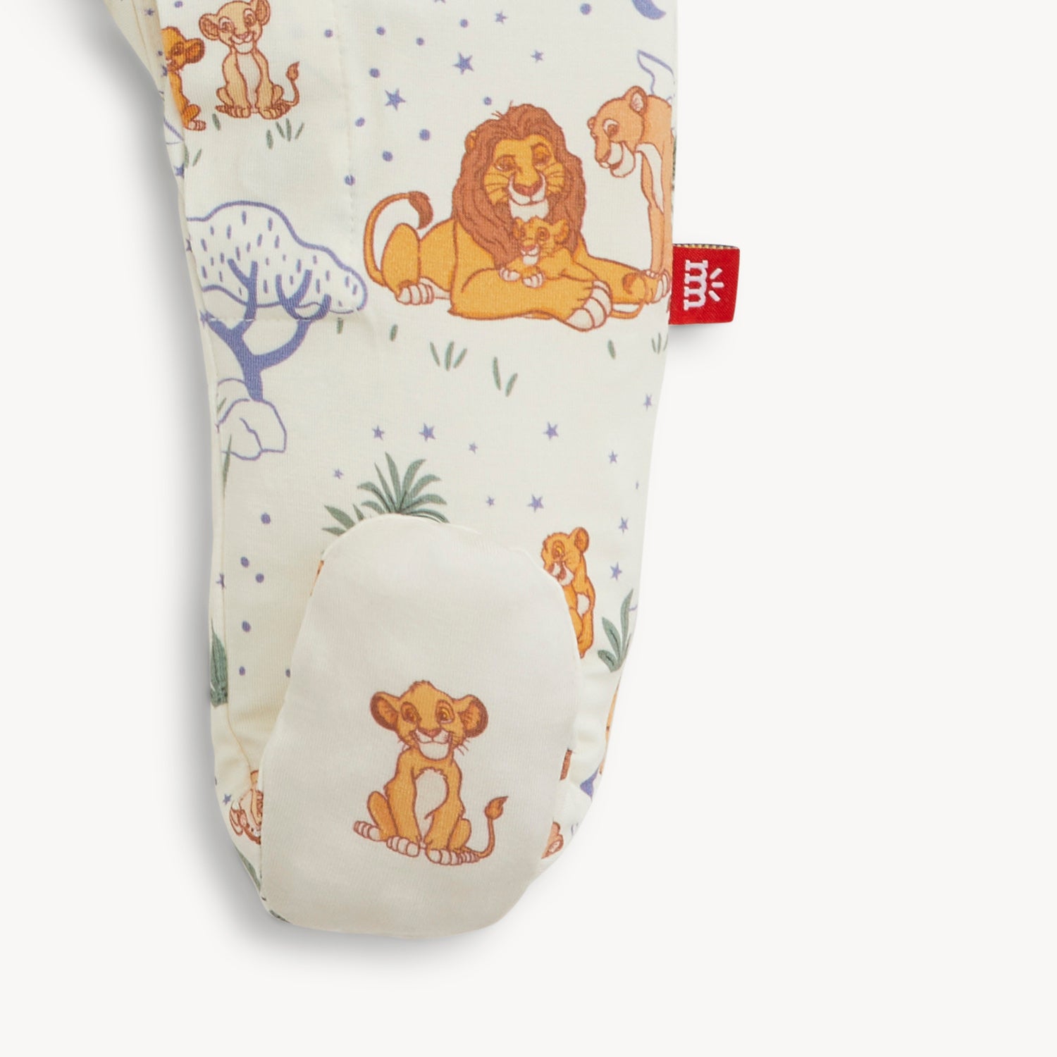 A close-up of a cream-colored footie featuring an all-over Disney Lion King savanna print with a digital graphic of a sitting Simba on the foot, by Magnetic Me