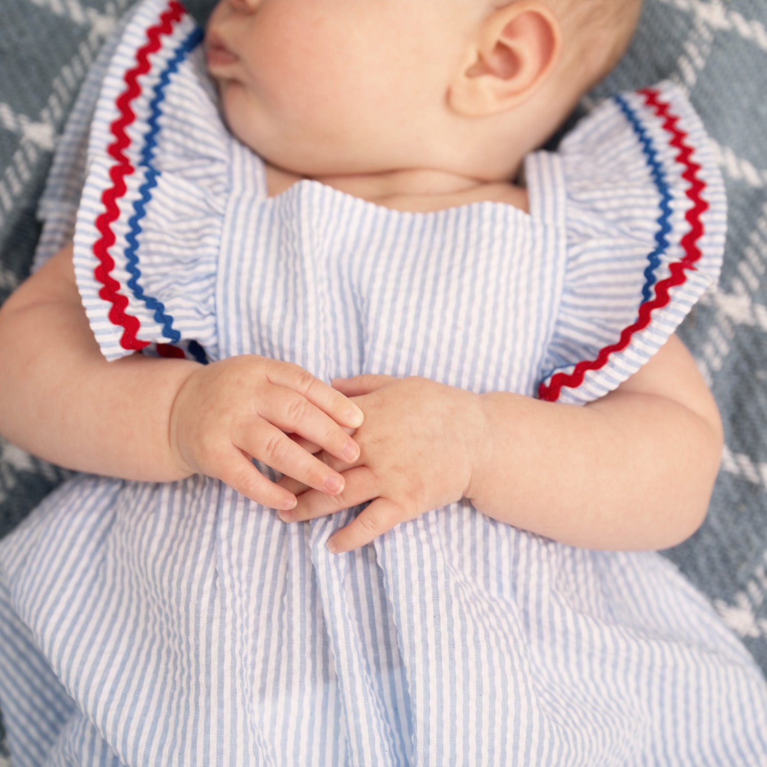 Baby sleeping on a blanket wearing A light blue striped seersucker bubble romper featuring ruffled shoulder straps accented with red and blue rickrack trim, by Magnetic Me.