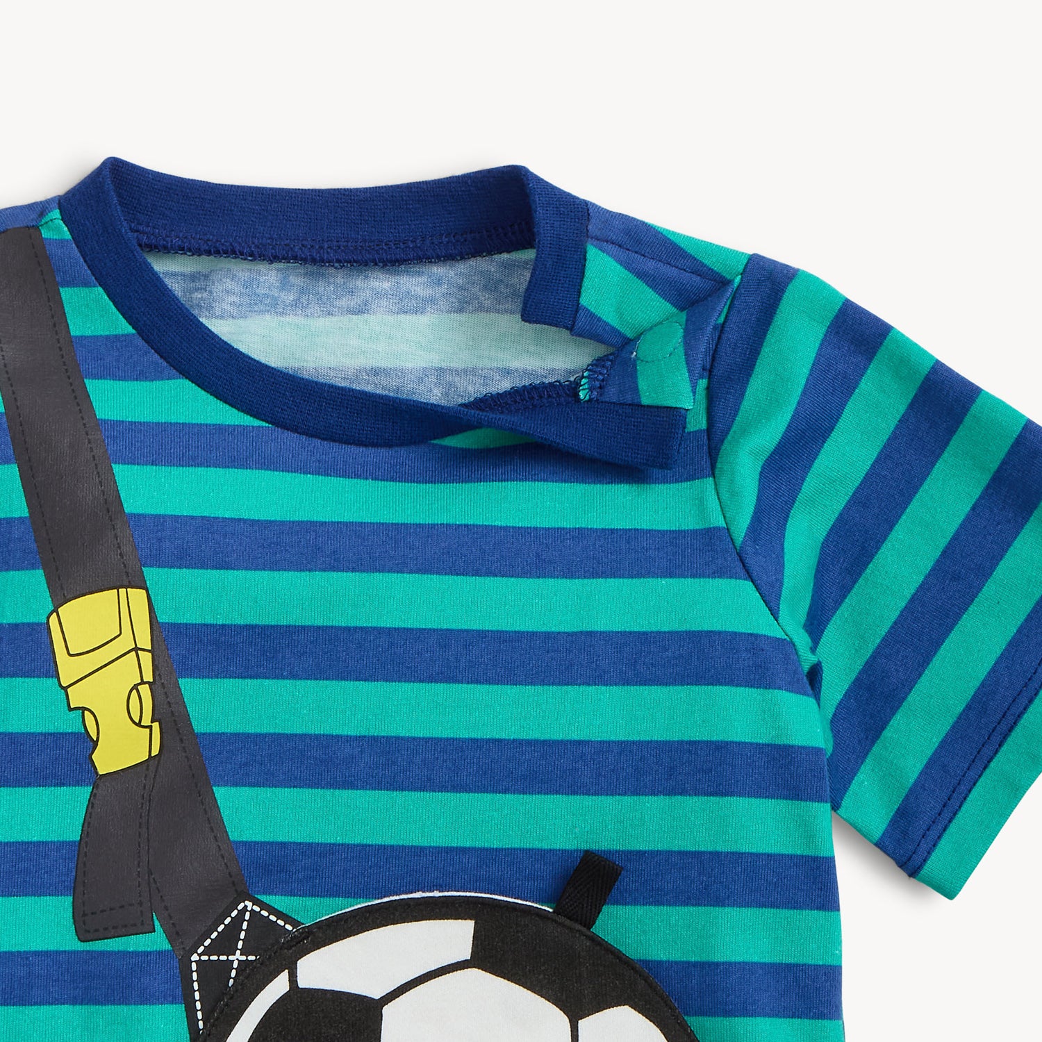 Close up of the open magnet of the sporty set features a teal and navy blue horizontally striped T-shirt with a large black and white soccer ball magnetic pocket on a printed black strap, paired with solid teal shorts, by Magnetic Me.