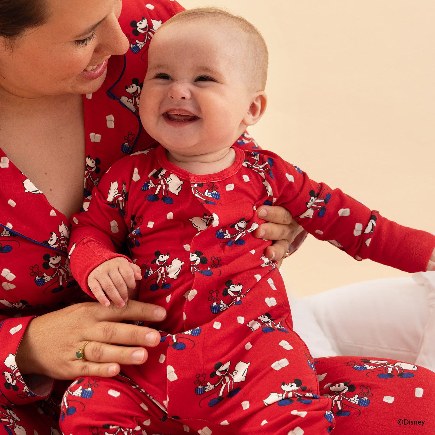 Woman and baby wearing matching red pajamas with cartoon characters on a beige background