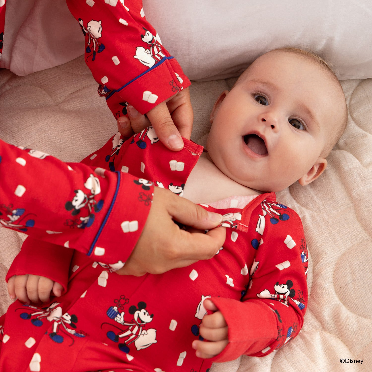 Adult opening the magnet on the baby wearing A vibrant red convertible coverall featuring a Disney-themed print of Mickey Mouse in striped pajamas holding a mug and pillow, accented with floating marshmallow motifs and a concealed magnetic closure for quick dressing by Magnetic Me.