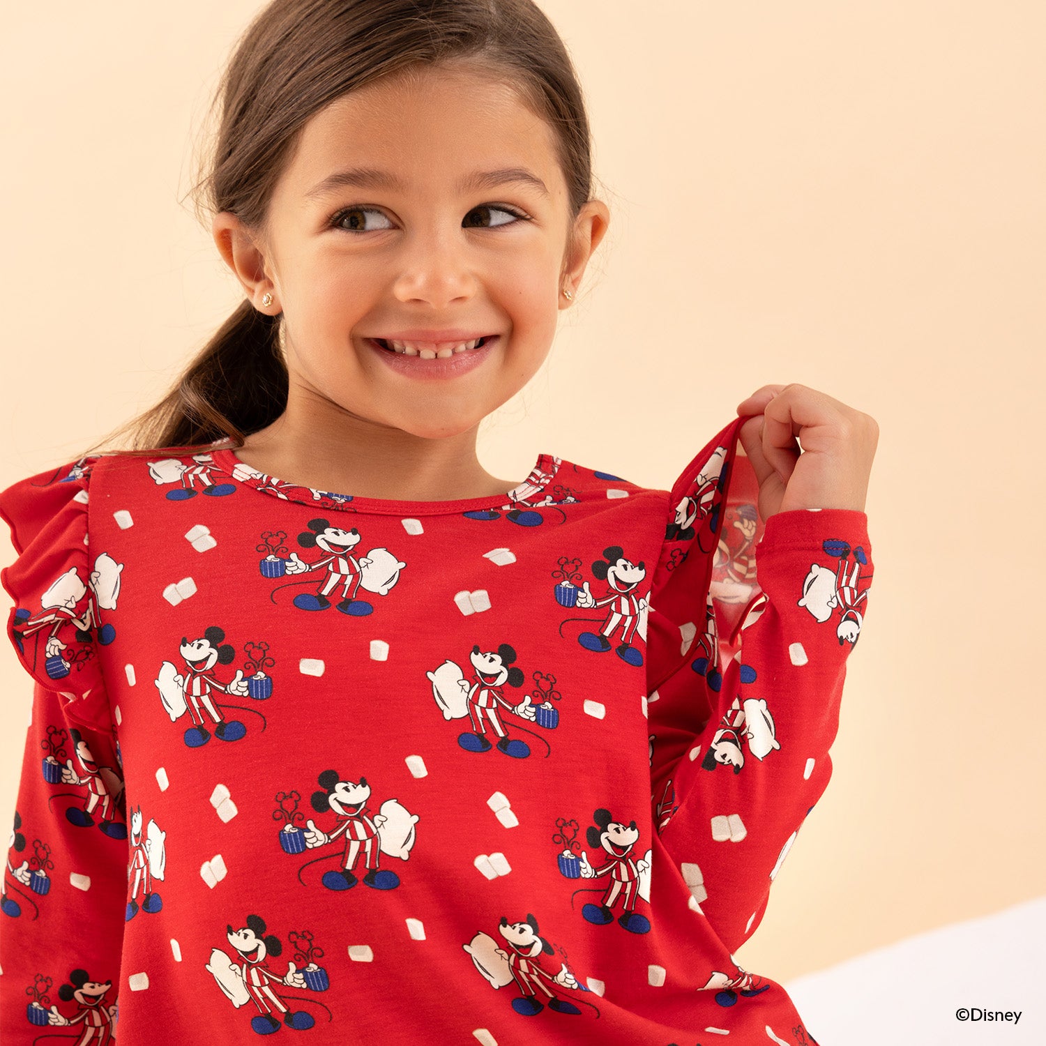 Girl opening the magnet on the shoulder of A vibrant red long-sleeve nightgown featuring a Disney print of Mickey Mouse in striped pajamas holding a mug and pillow, detailed with ruffle trim at the shoulders and hem by Magnetic Me.