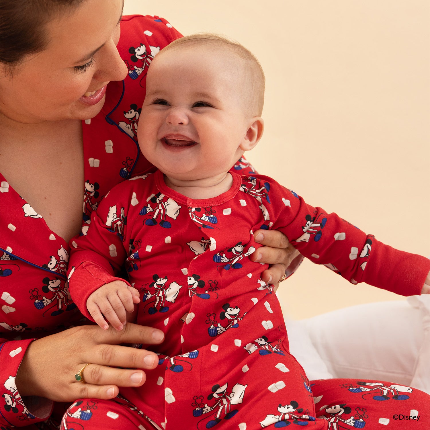 Woman and baby wearing red pajamas with Disney Mickey characters on a beige background