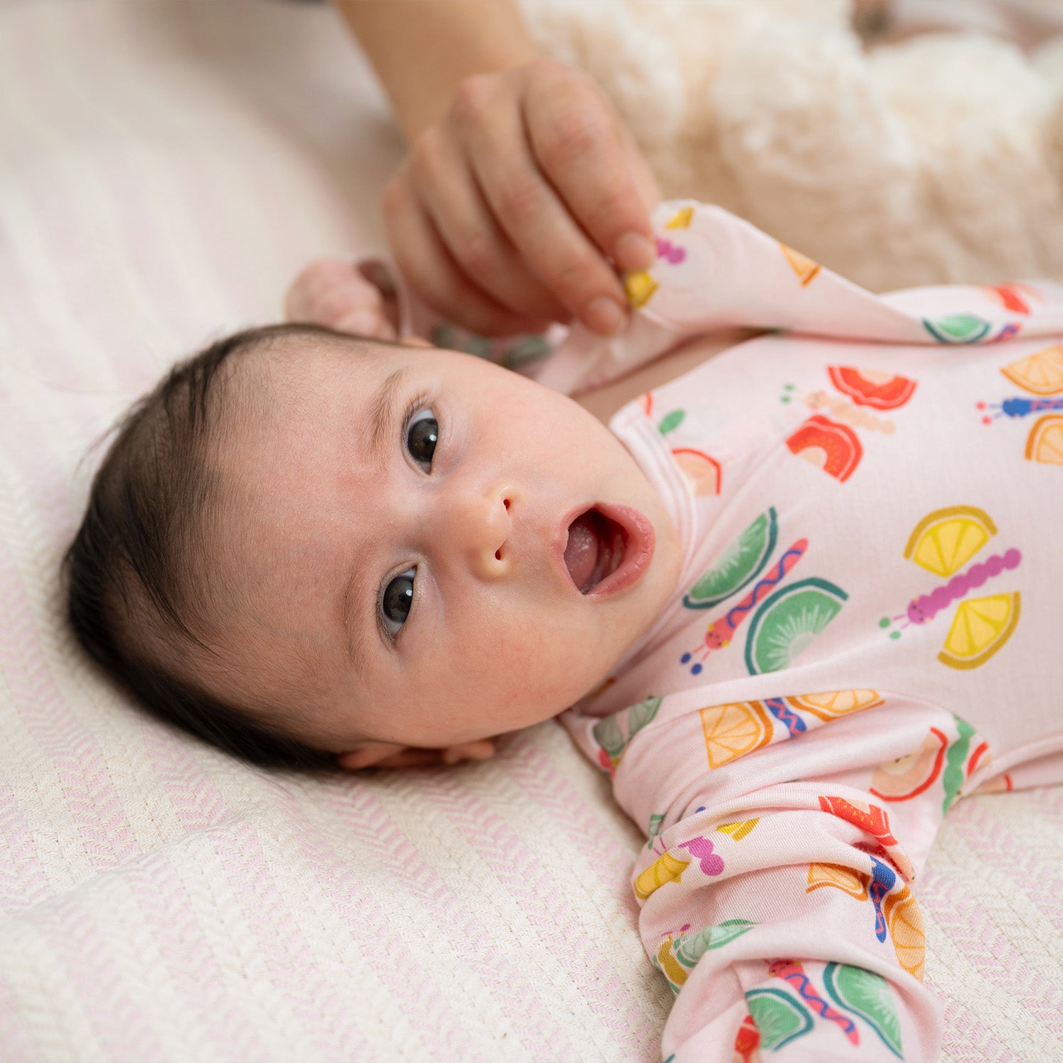Baby  lying on a soft surface wearing A light pink long-sleeve footie featuring an all-over print of colorful butterflies with fruit-slice wings, by Magnetic Me.