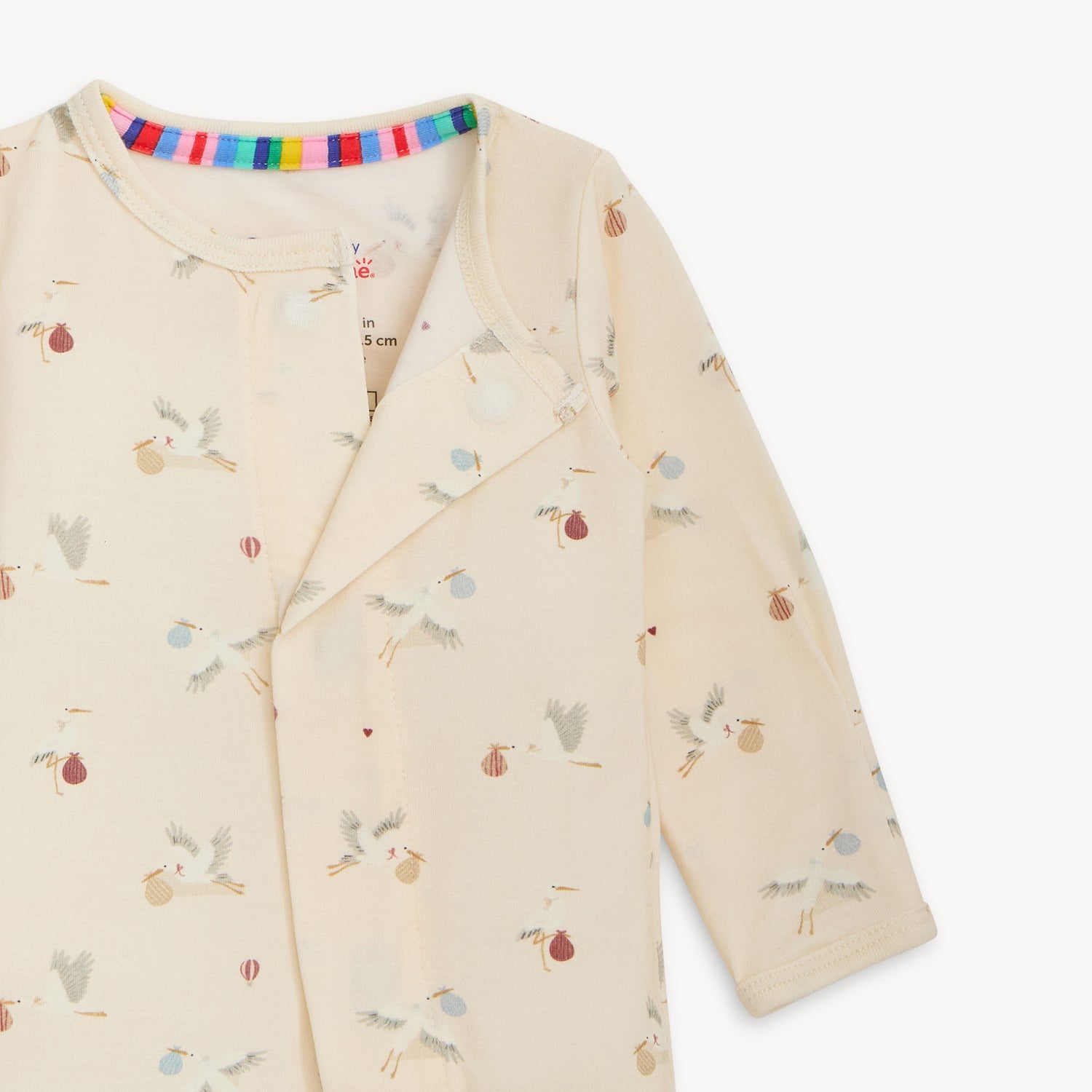 Open magnet of A cream-colored long-sleeve footed infant romper featuring a whimsical all-over print of flying storks carrying colorful bundles, by Magnetic Me.
