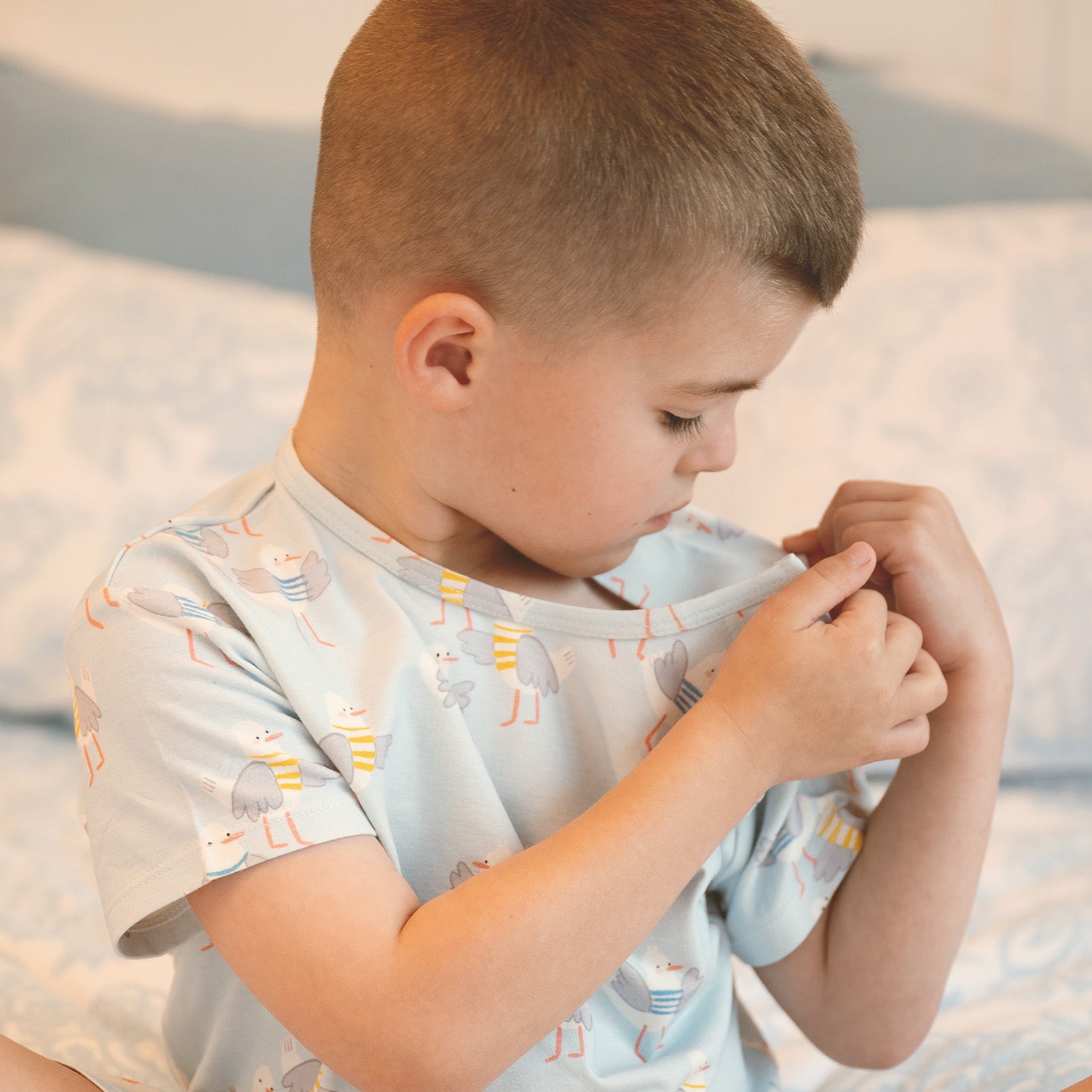 Child opening the magnet of A two-piece children's pajama set including a short-sleeved top and matching shorts in light blue with an all-over seagull sweater print, by Magnetic Me.
