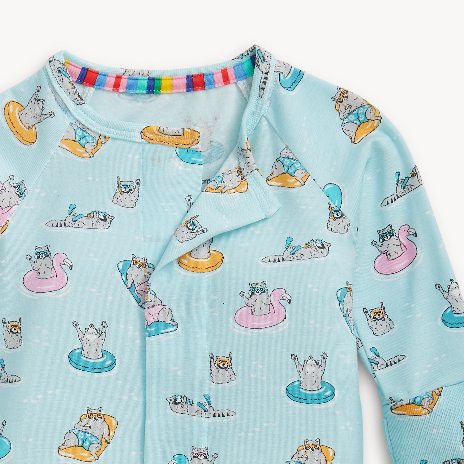 Open magnet in the center front of A light blue convertible coverall with a whimsical pattern of raccoons relaxing on pool rafts and swimming, by Magnetic Me.