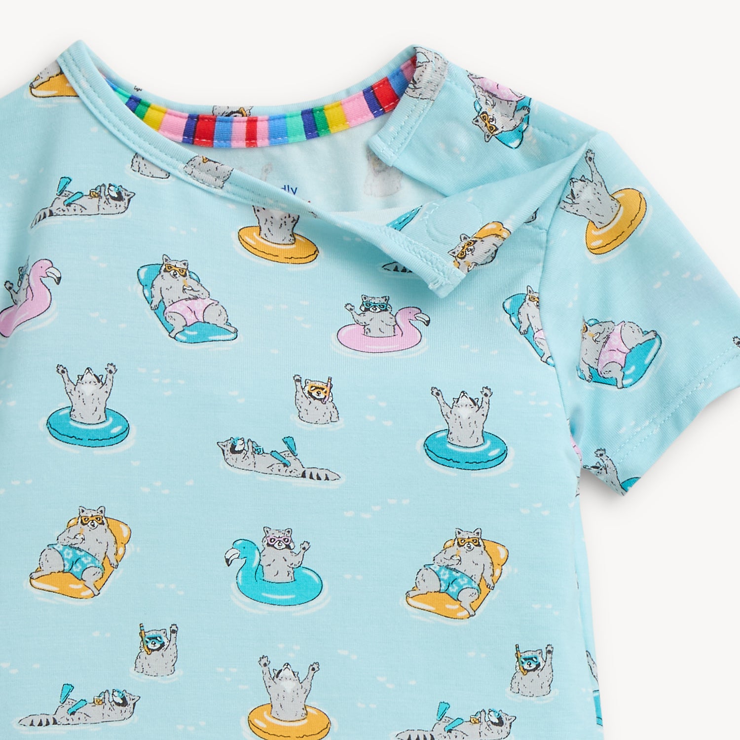 Open magnet by the shoulder area of A two-piece pajama set in light blue featuring a repeating print of raccoons on bright pool floats and wearing goggles, by Magnetic Me.
