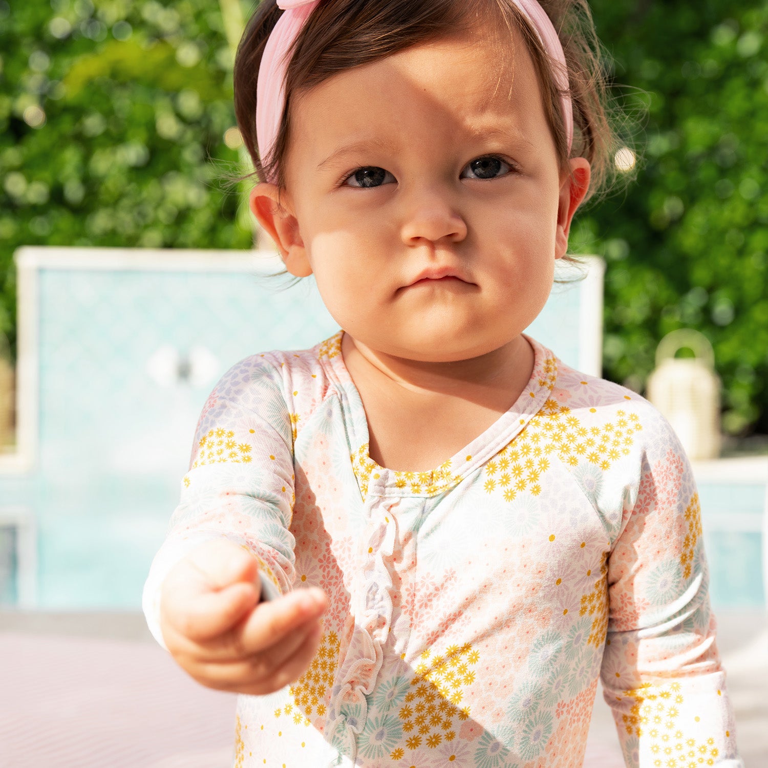 Child standing outdoors wearing A long-sleeve convertible coverall with ruffle detailing and a multi-colored pastel floral pattern, by Magnetic Me.