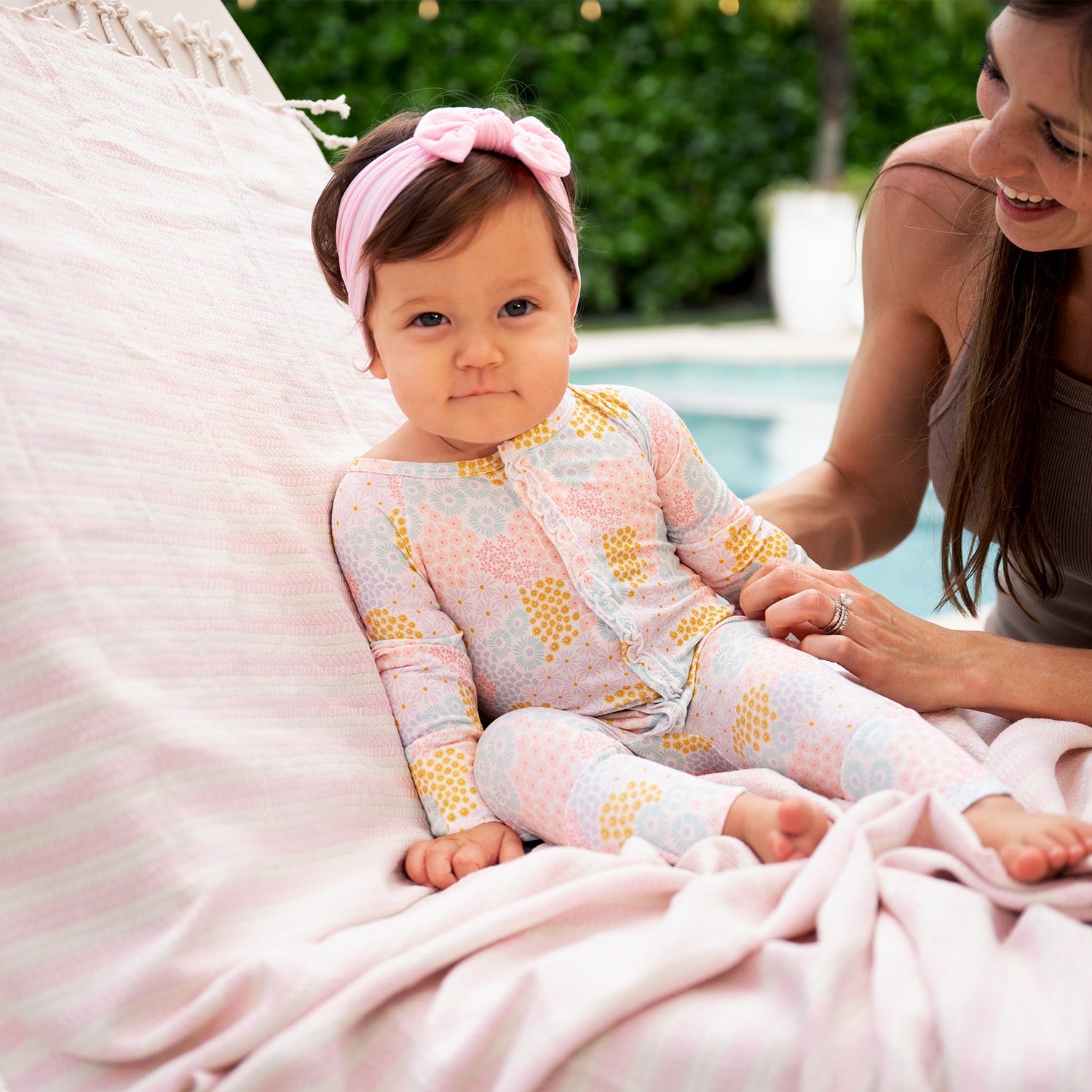 Baby sitting on a pink blanket with a woman next to her and wearing A long-sleeve convertible coverall with ruffle detailing and a multi-colored pastel floral pattern, by Magnetic Me.