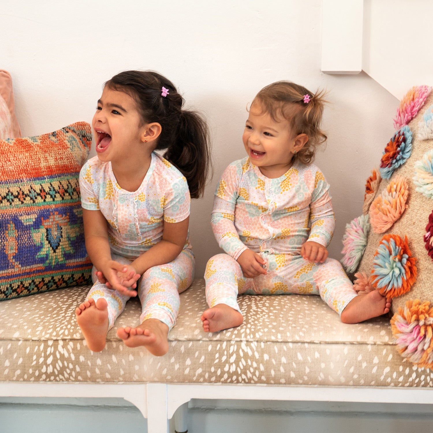 Two children in matching two-piece pajama set featuring a short-sleeve ruffle-trim top and matching pants in a bright pastel spring floral print, by Magnetic Me.