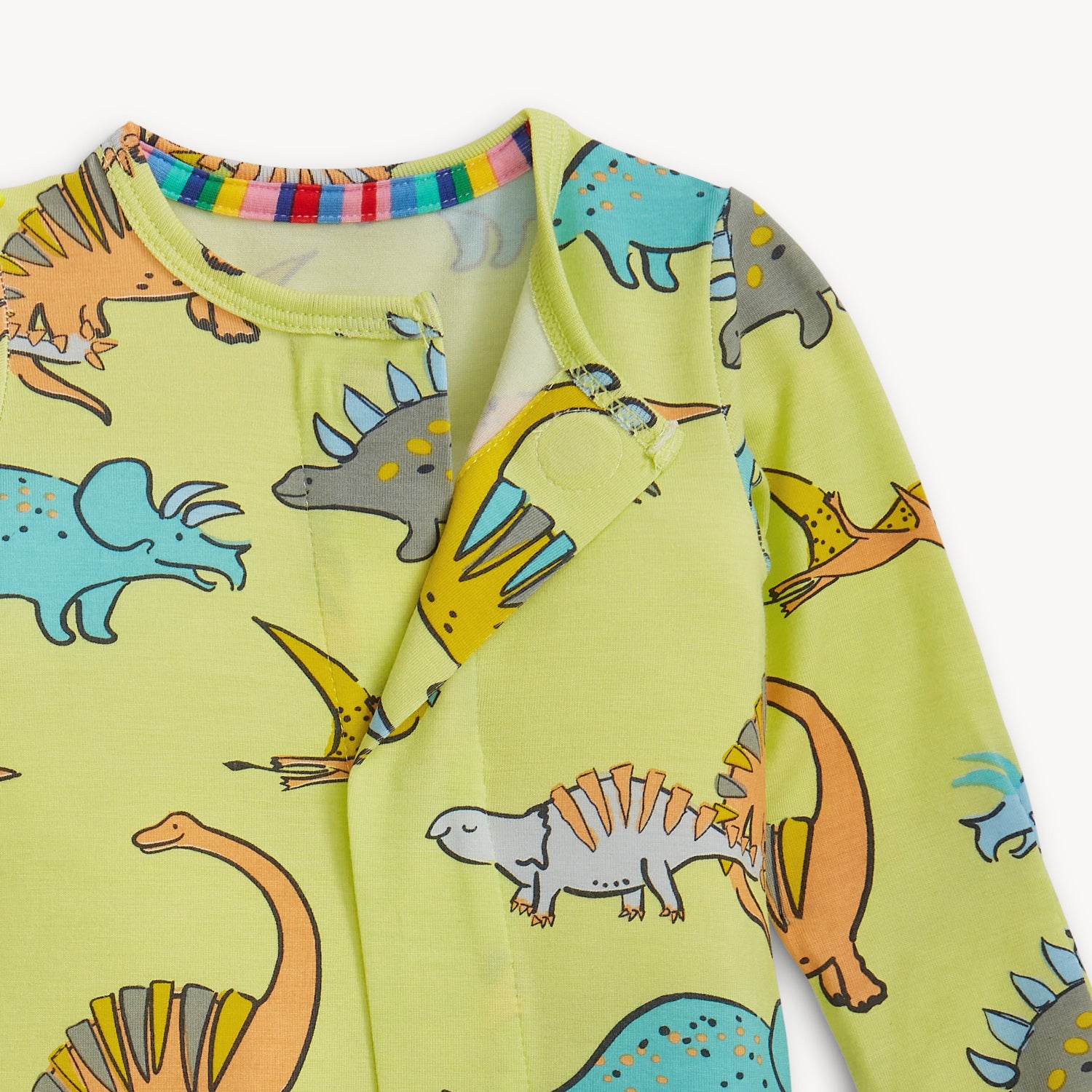 Open magnet in the front center of A long-sleeve footie in lime green featuring a colorful repeating print of various dinosaurs like triceratops and apatosaurus, by Magnetic Me.