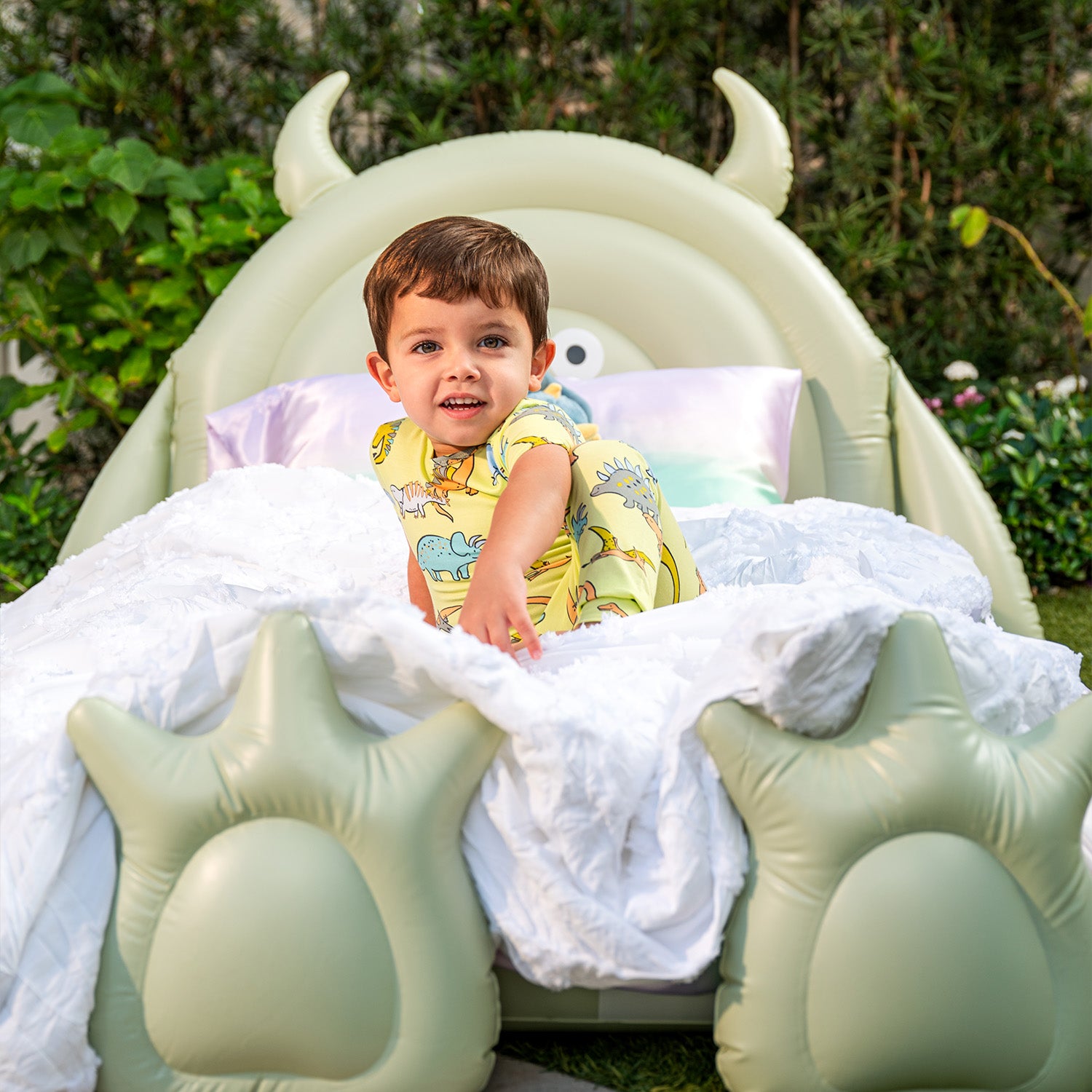 Child sitting in a green inflatable dragon-shaped bed wearing A two-piece pajama set with a short-sleeve top and long pants in lime green fabric covered in a whimsical dinosaur print, by Magnetic Me.