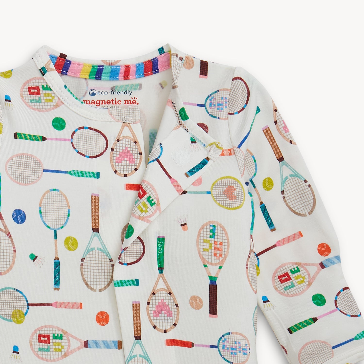 Open magnet in the center front of A long-sleeve cream footie featuring a playful, multi-colored pattern of tennis rackets, balls, and badminton shuttlecocks, by Magnetic Me.