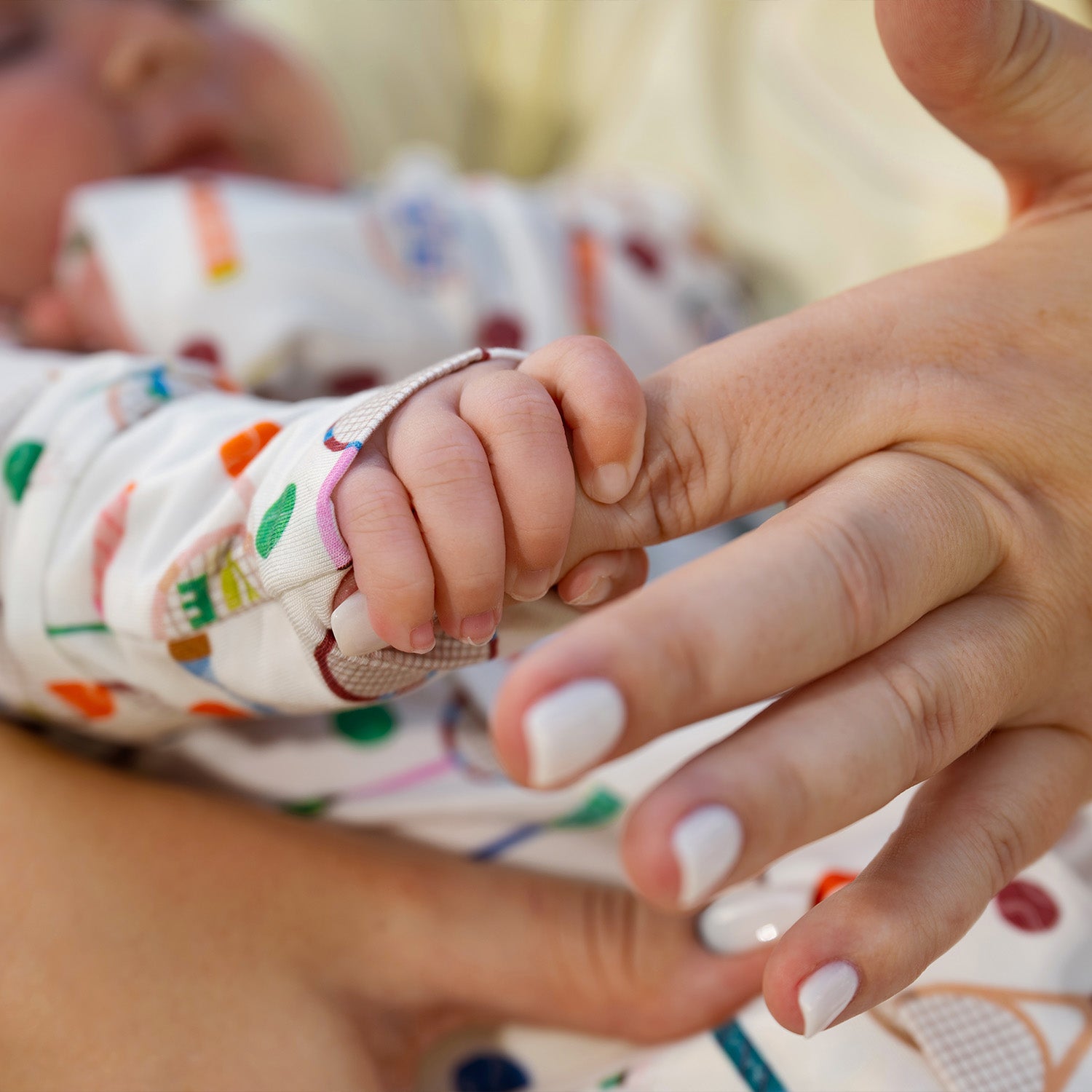 Close-up of a baby's hand holding an adult's finger with a blurred background