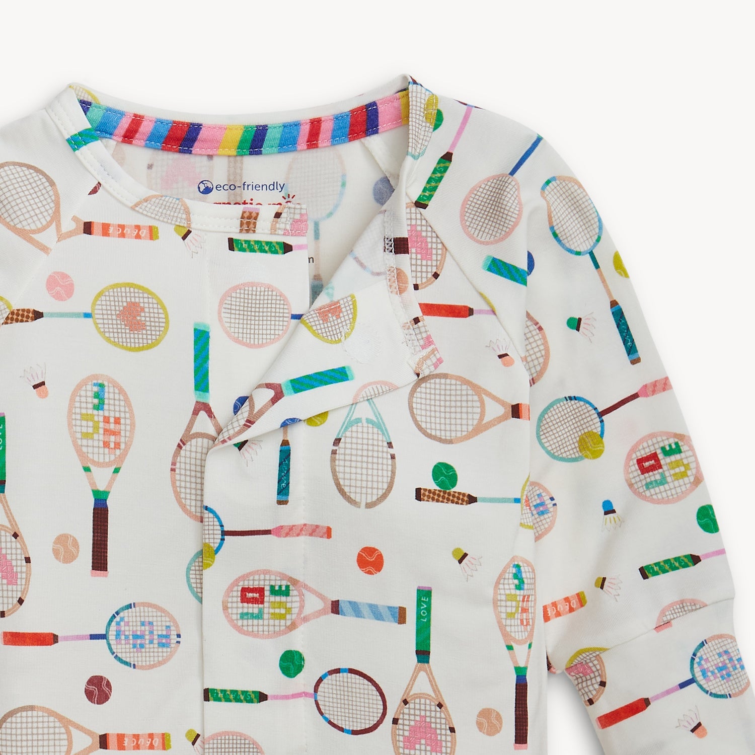 Open magnet in the center front of A cream-colored long-sleeve convertible coverall with a colorful repeating print of sports rackets and tennis balls, by Magnetic Me.