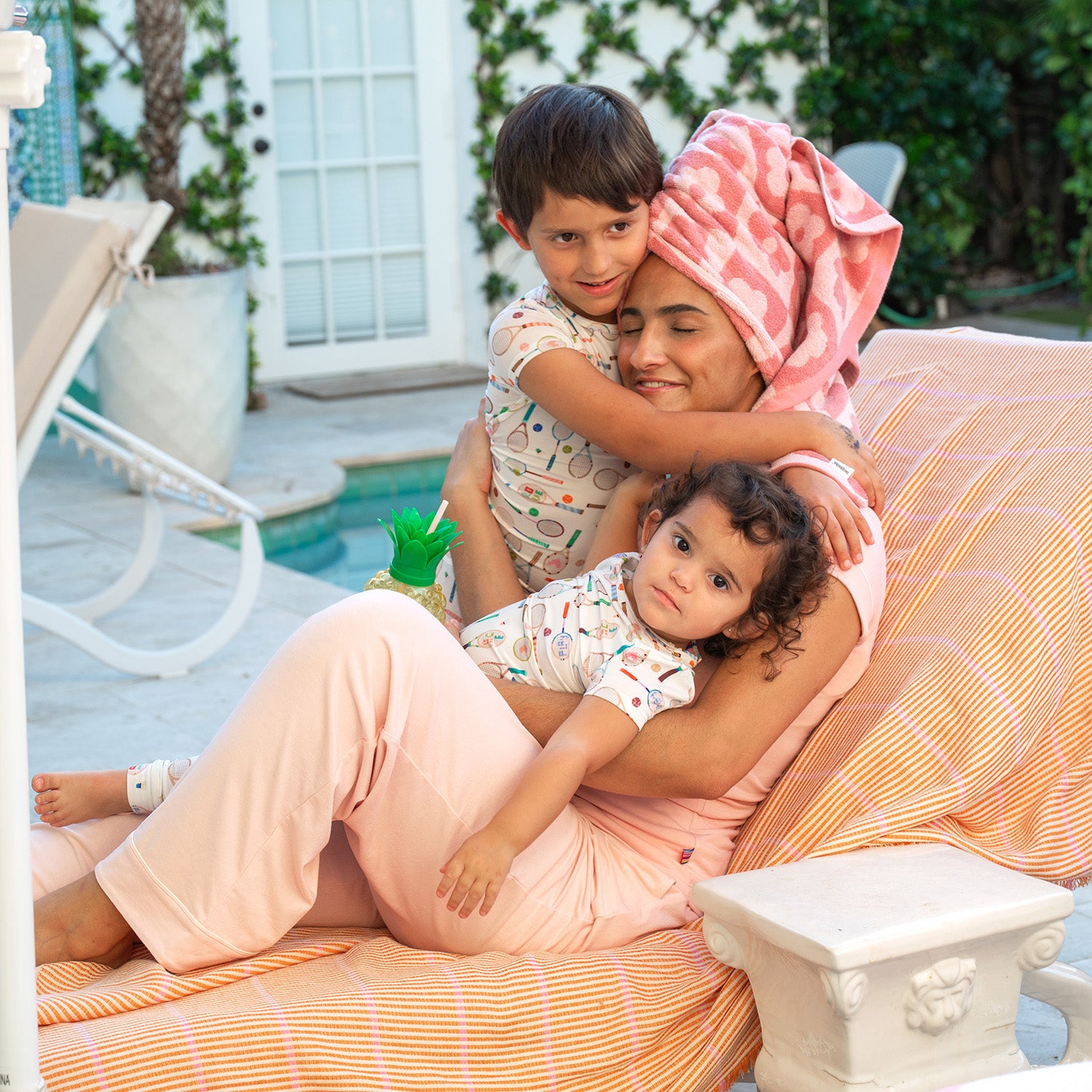 Woman sitting on a chair with two children, one on each lap, in an outdoor setting, by Magnetic Me.