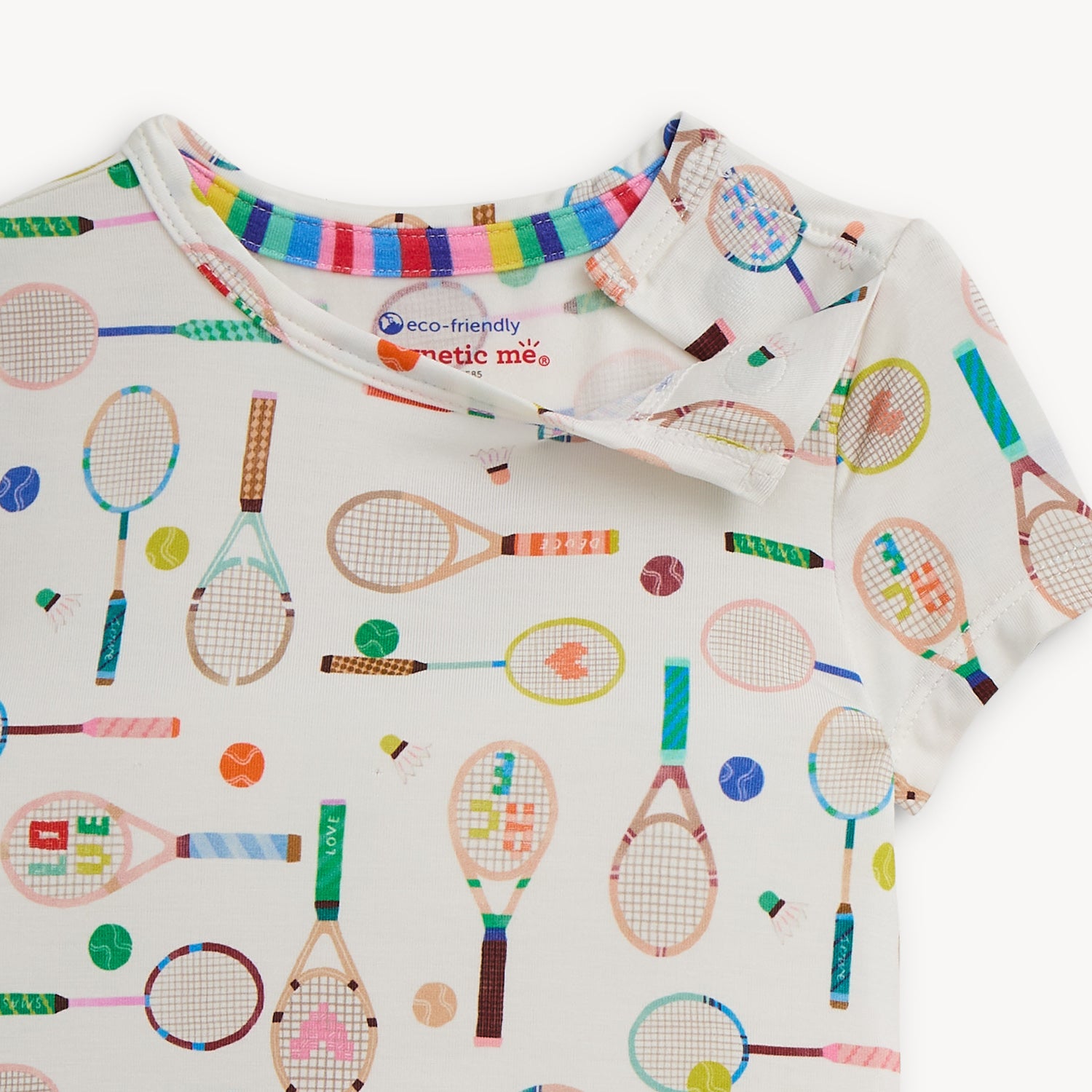 Open magnet on the shoulder area of A two-piece pajama set with a cream short-sleeve top and long pants covered in a whimsical tennis and badminton equipment print, by Magnetic Me.