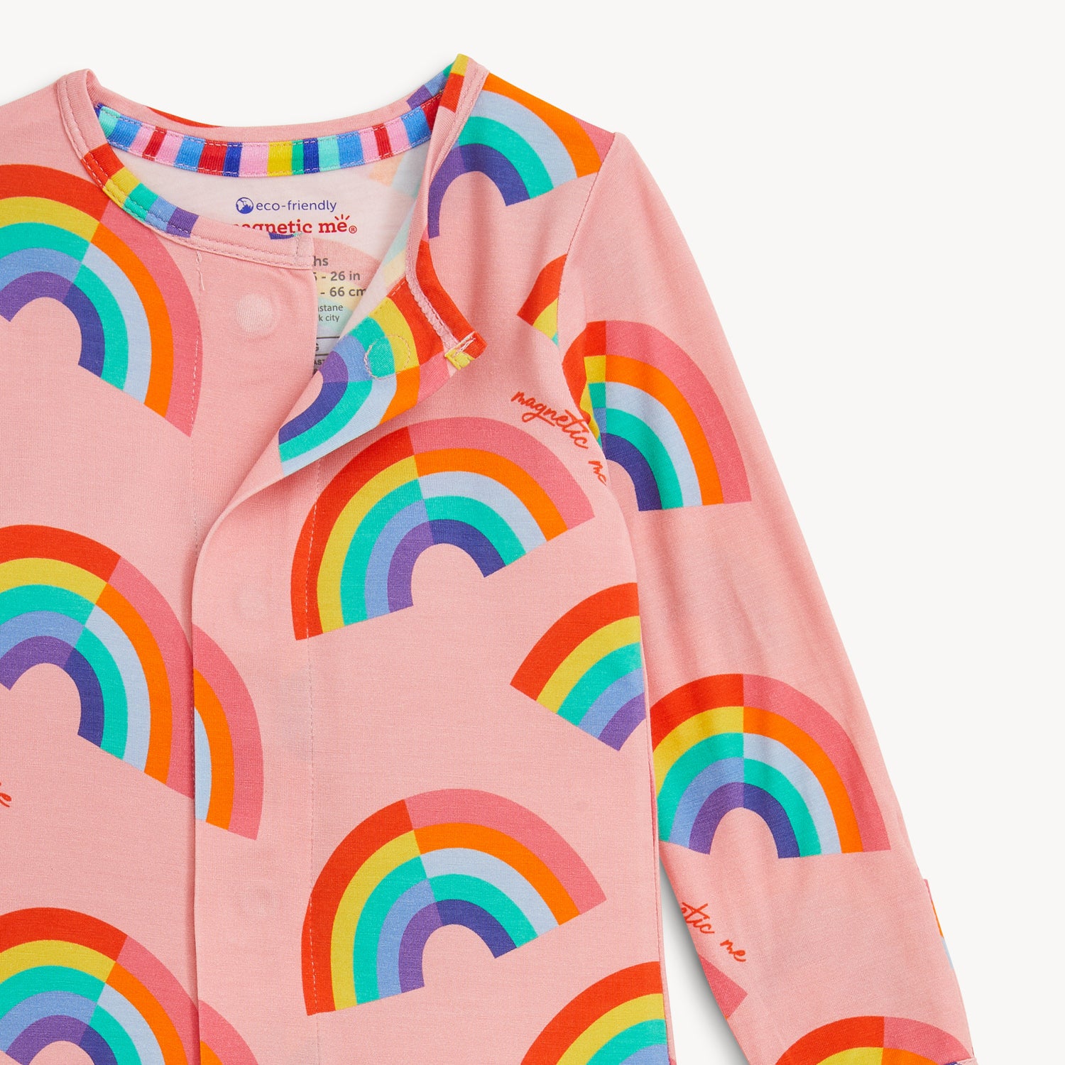 Open magnet in the center front of A long-sleeve pink footie featuring a repeating pattern of vibrant, multi-colored rainbows, by Magnetic Me.