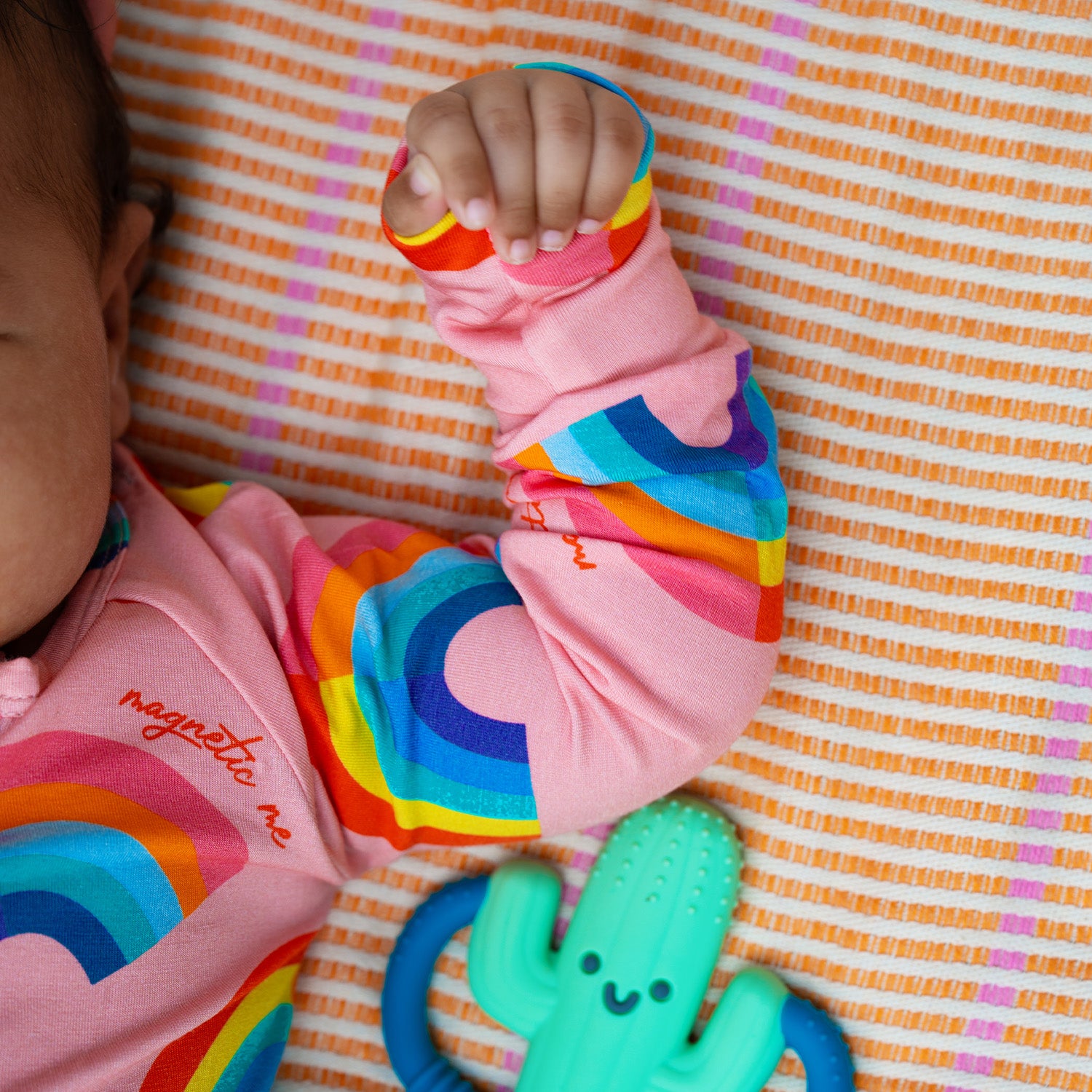Close up of the baby arm of the pink long-sleeve convertible coverall decorated with a colorful all-over rainbow print and ribbed cuffs, by Magnetic Me.