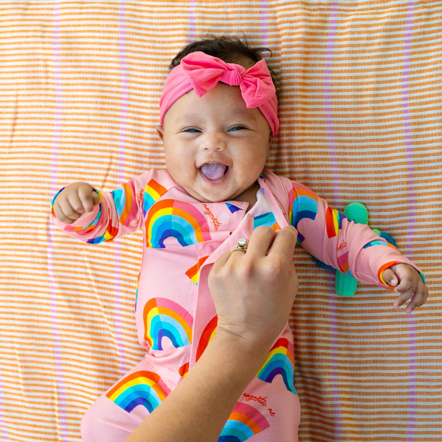 Baby in a pink rainbow and A pink long-sleeve convertible coverall decorated with a colorful all-over rainbow print and ribbed cuffs, by Magnetic Me.