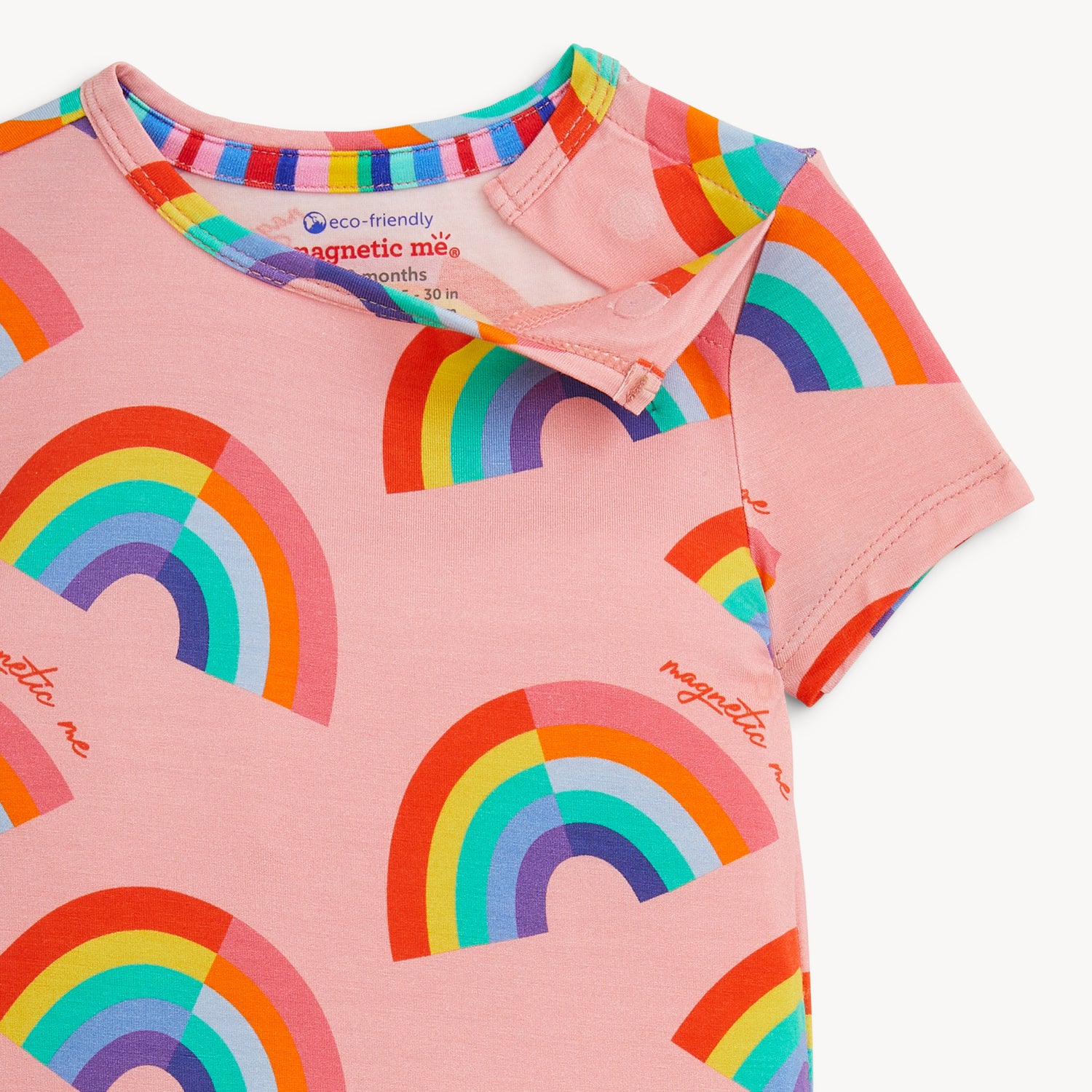Open magnet on the shoulder side of A two-piece pajama set with a short-sleeve top and matching shorts in pink fabric featuring a bright, repeating rainbow pattern, by Magnetic Me.
