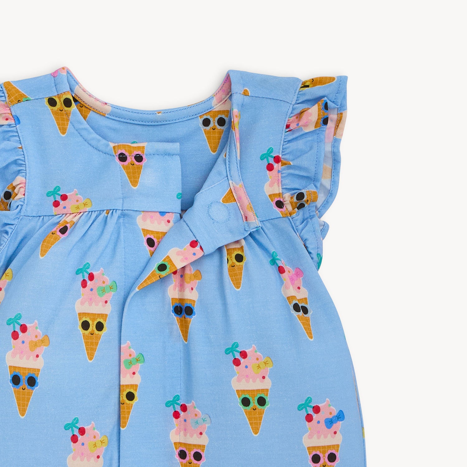 Open magnet in the center of the cornflower blue sleeveless romper with ruffled flutter sleeves and cinched leg openings, featuring a charming ice cream cone character print, by Magnetic Me.