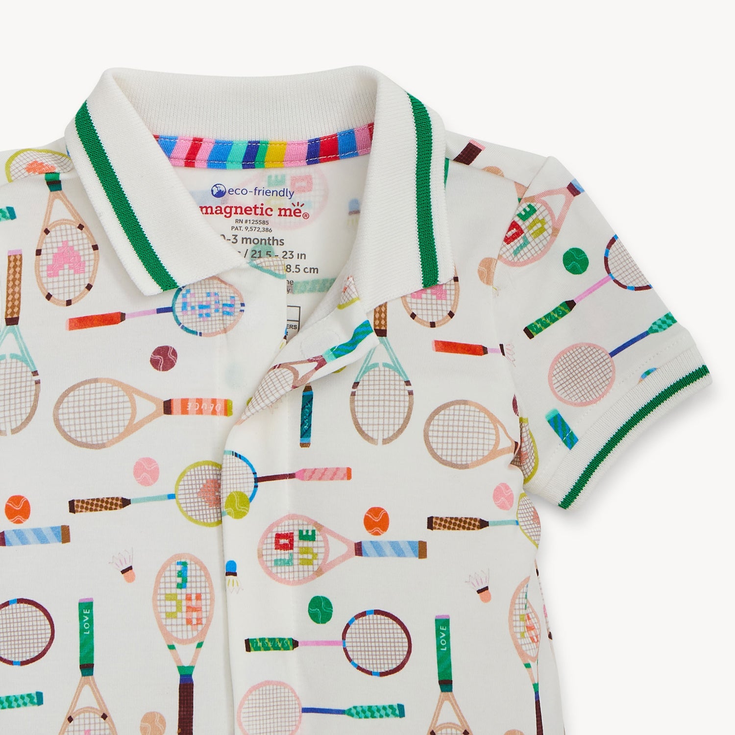 Open magnet beneath the polo collar of A cream-colored short-sleeve romper with a green-trimmed polo collar, featuring a repeating print of tennis rackets, shuttlecocks, and colorful sports balls, by Magnetic Me.