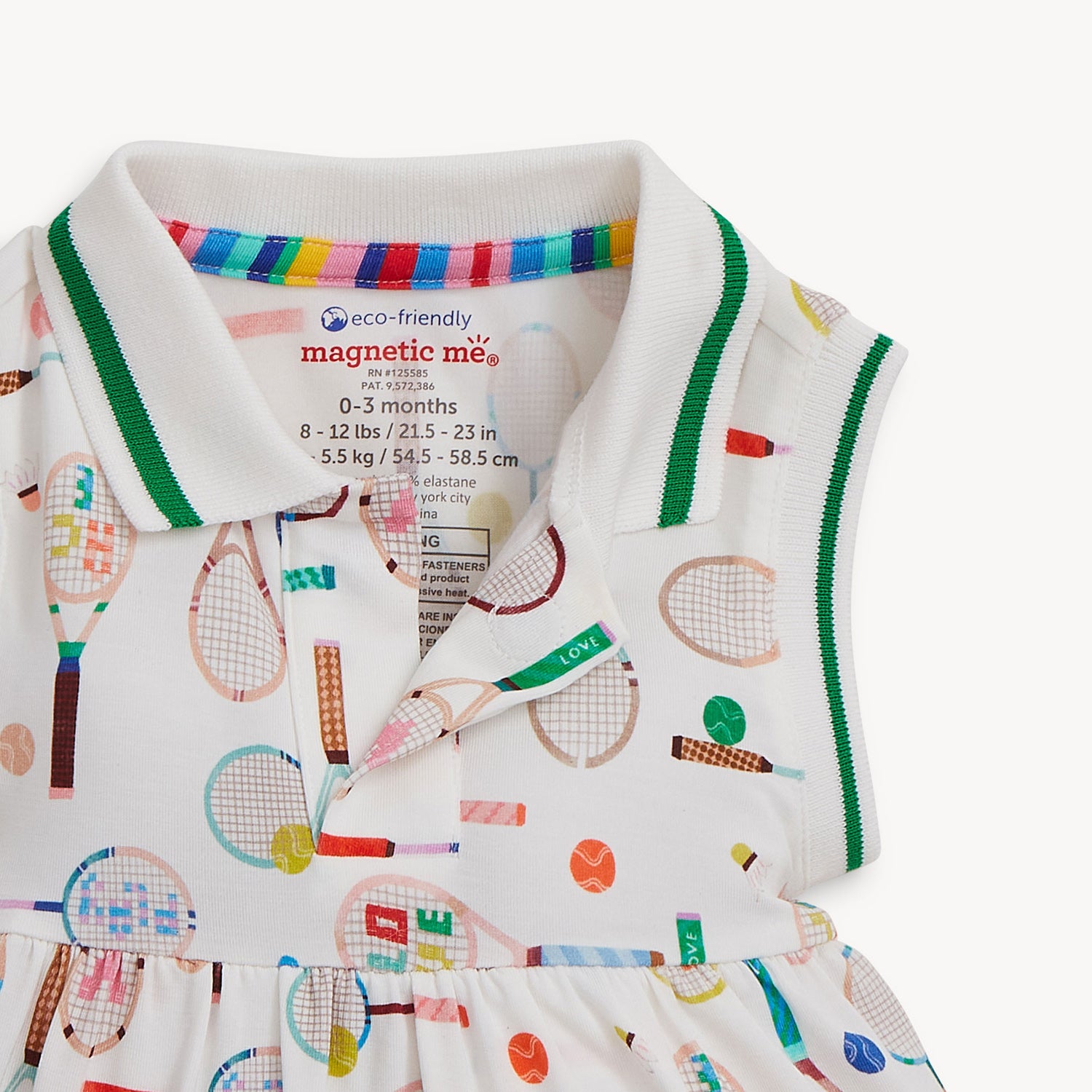 Open magnet on the bottom of the collar of A sleeveless cream-colored dress with a pink-trimmed polo collar and an integrated bodysuit, featuring a colorful print of tennis rackets, balls, and shuttlecocks, by Magnetic Me.