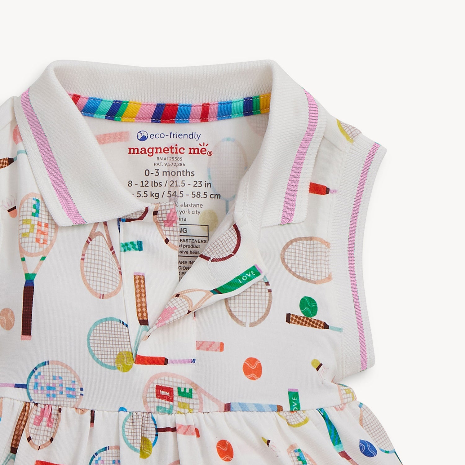 Open magnet on the bottom of the collar of A sleeveless cream-colored dress with a pink-trimmed polo collar and an integrated bodysuit, featuring a colorful print of tennis rackets, balls, and shuttlecocks, by Magnetic Me.