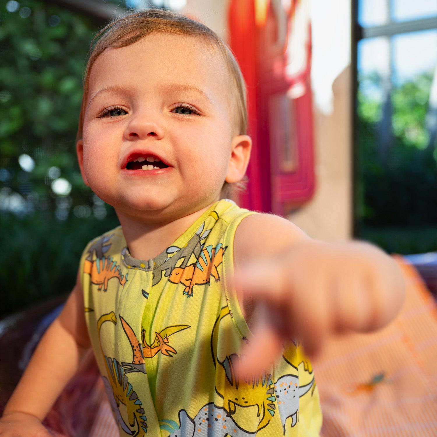 Child pointing forward outdoors and wearing A sleeveless one-piece romper in lime green with a vibrant all-over print of prehistoric dinosaurs and flying pterodactyls, by Magnetic Me.