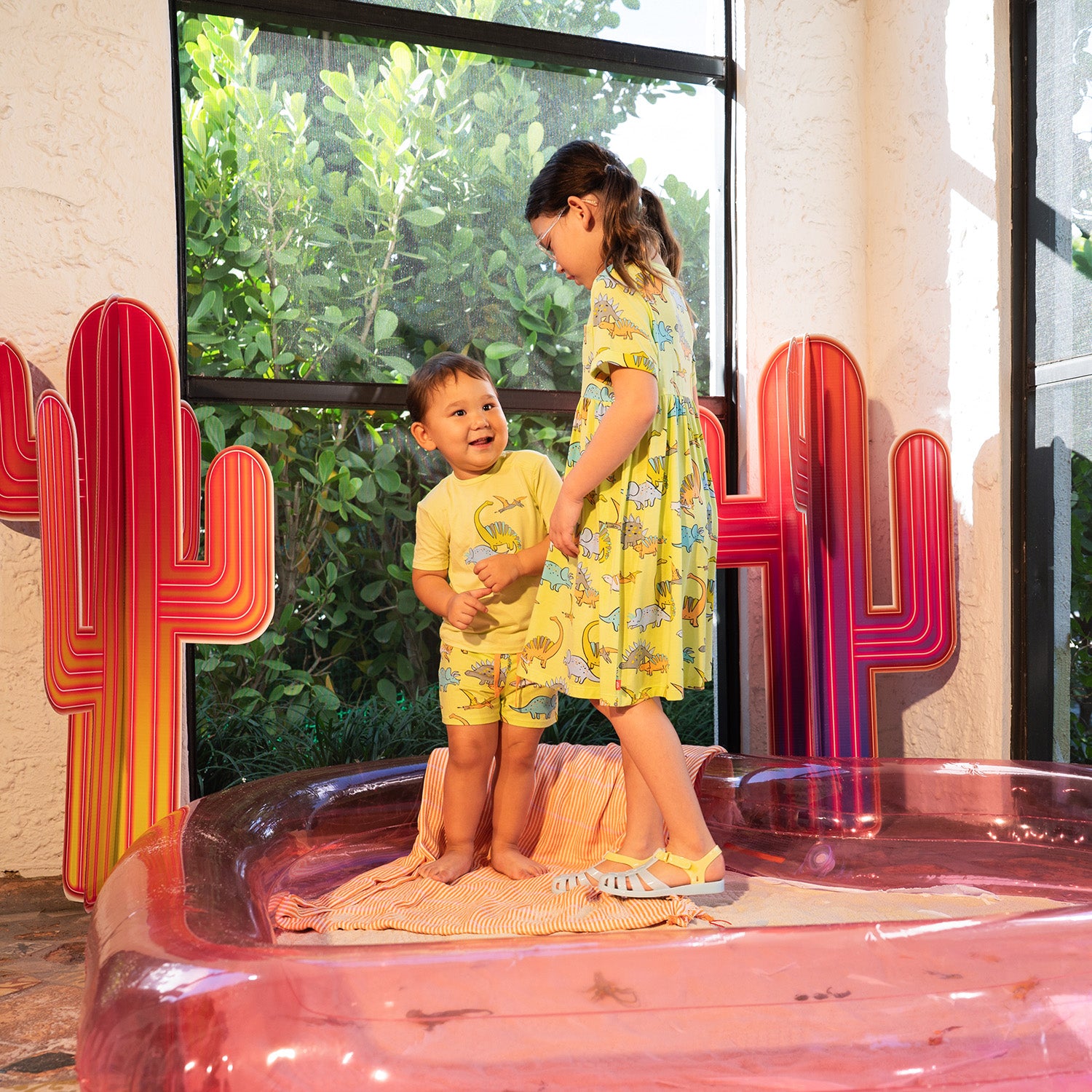 Two children in matching Roar & Explore outfits standing on a pink platform with red cactus decorations.