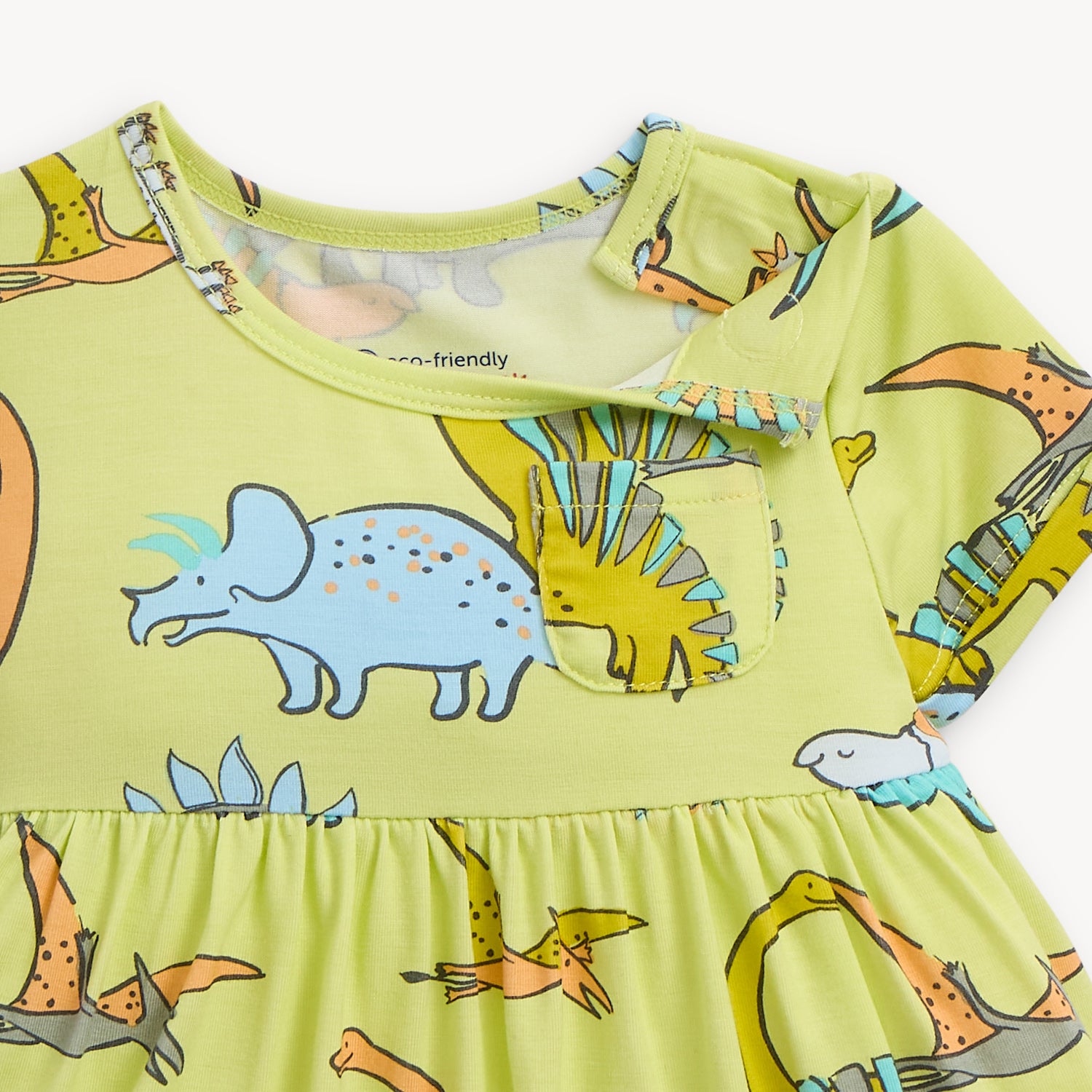 Open magnet on the shoulder area of A lime green short-sleeve infant dress with a gathered waist, small chest pocket, and an integrated bodysuit featuring a colorful dinosaur pattern, by Magnetic Me.