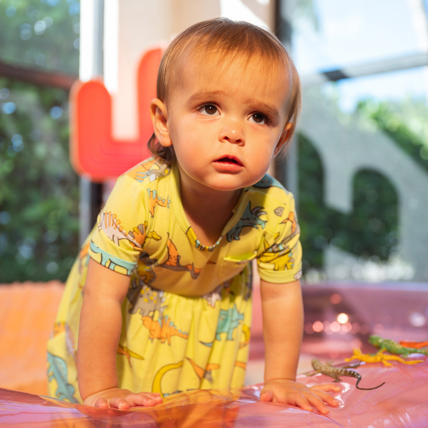 Child on an inflatable pool wearing A lime green short-sleeve infant dress with a gathered waist, small chest pocket, and an integrated bodysuit featuring a colorful dinosaur pattern, by Magnetic Me.