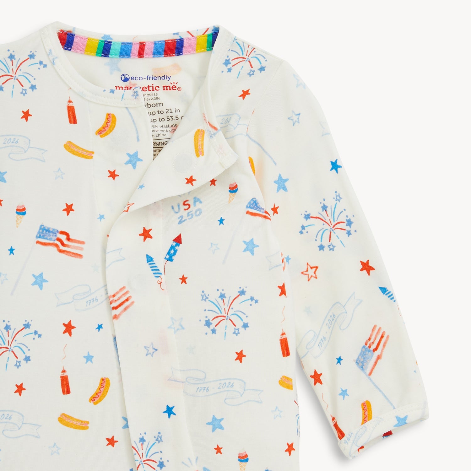 Open magnet in the front center of A long-sleeve white footie featuring a patriotic Fourth of July print of American flags, fireworks, hot dogs, and "USA 250" text, by Magnetic Me.