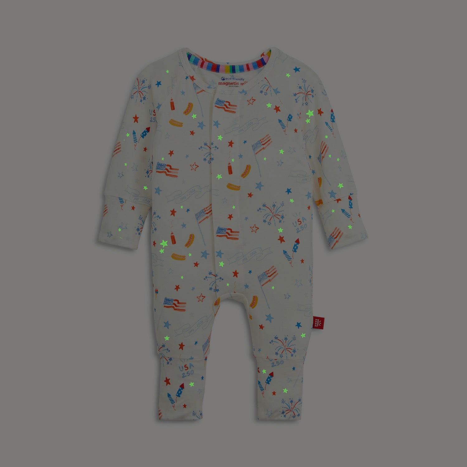 Glow in the dark white long-sleeve convertible coverall decorated with a festive repeating print of stars, banners, and picnic foods, by Magnetic Me.