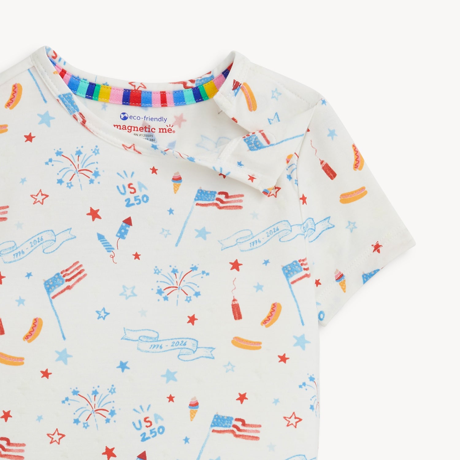 Open magnet on the shoulder side of A two-piece white pajama set with a short-sleeve top and shorts featuring a colorful celebratory print of rockets and "1776-2026" banners, by Magnetic Me.