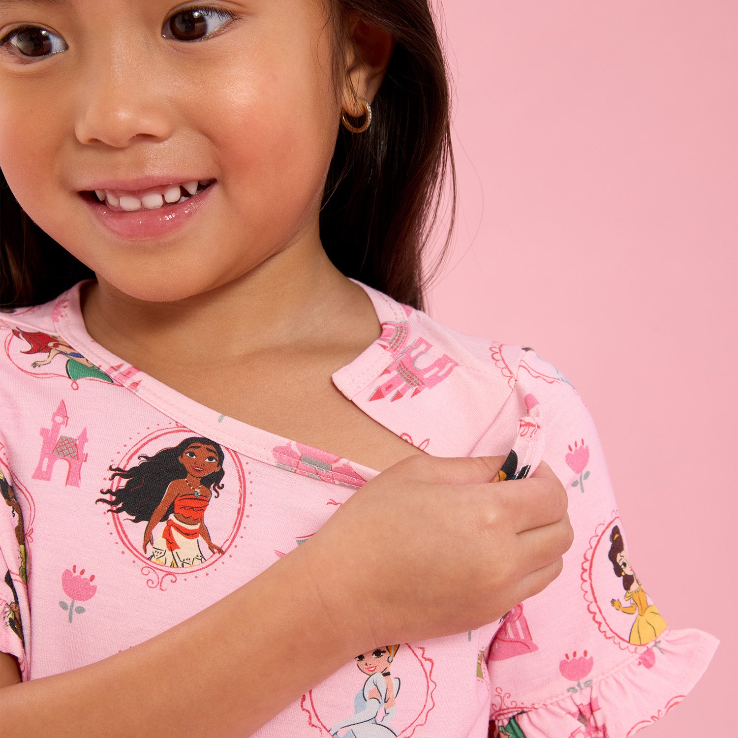 Girl opening he magnet of A pink short-sleeve nightgown with flutter sleeves and a ruffled hem featuring an all-over print of Disney Princesses Ariel, Belle, Moana, Tiana, Jasmine, and Cinderella, by Magnetic Me.