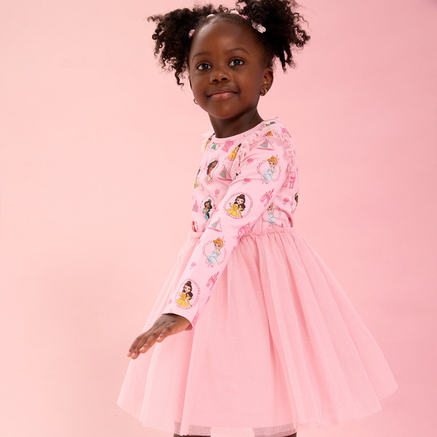 Young girl wearing A pink short-sleeve nightgown with flutter sleeves and a ruffled hem featuring an all-over print of Disney Princesses Ariel, Belle, Moana, Tiana, Jasmine, and Cinderella, by Magnetic Me.