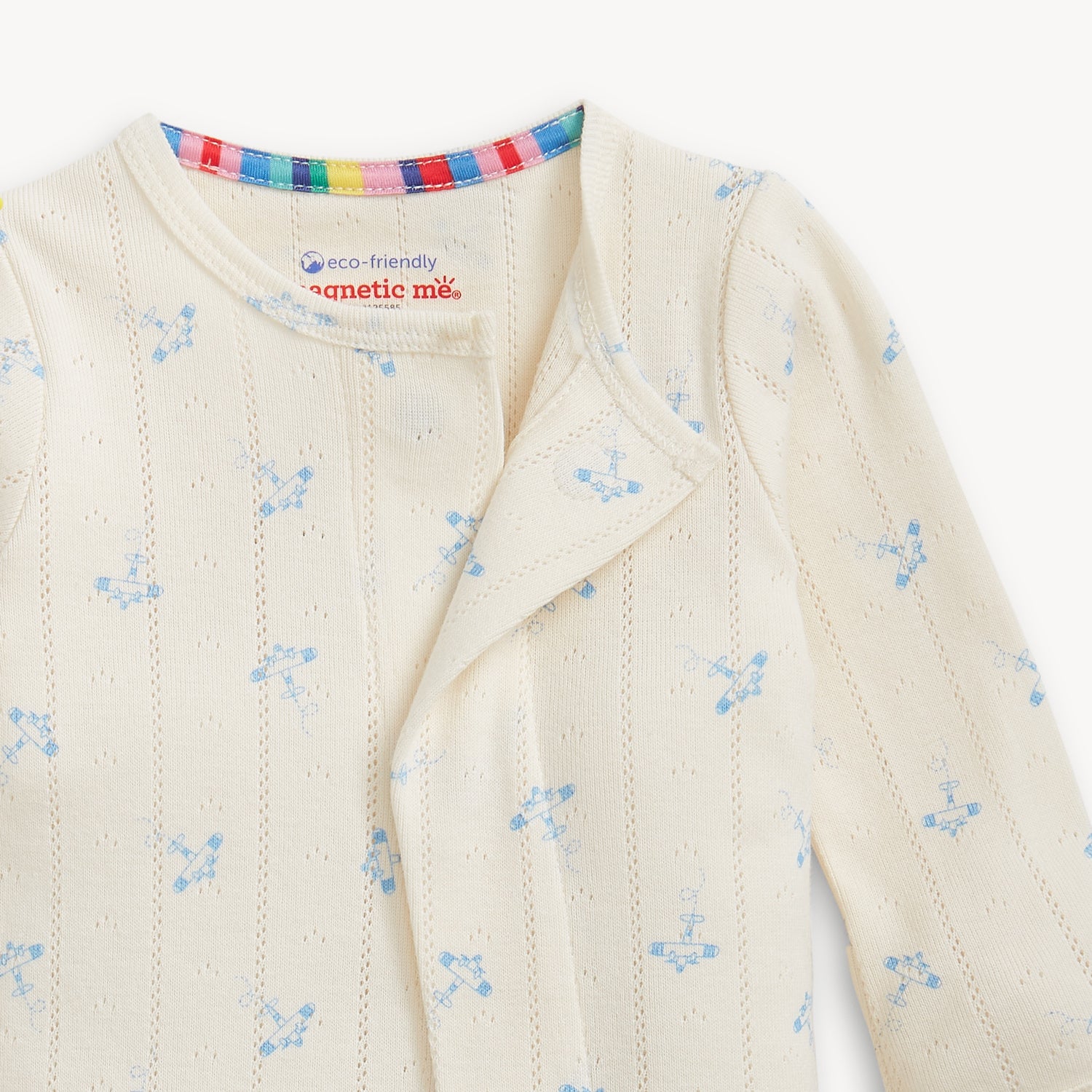 Open magnet close up of A cream-colored pointelle long-sleeve footie with a subtle blue airplane pattern and magnetic closures, by Magnetic Me.