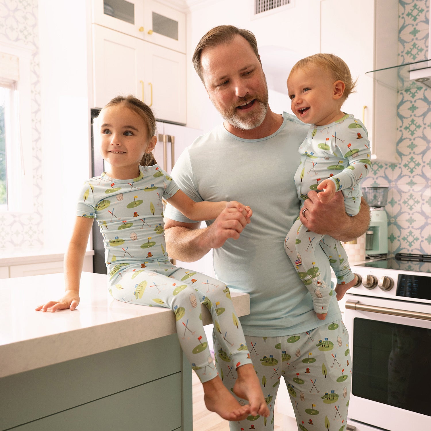 Man and two children in matching light blue pajama set with green golf patterned print in a kitchen