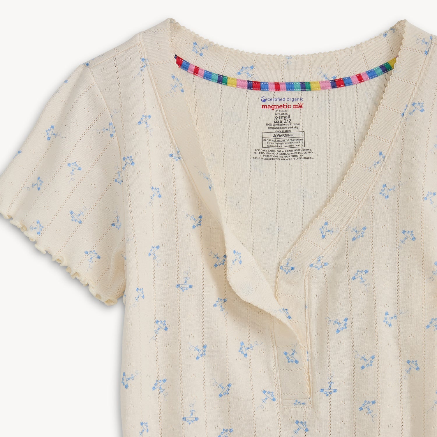 Open magnet close up of A cream-colored pointelle short-sleeve top and matching long pants set featuring a delicate blue airplane print, by Magnetic Me.