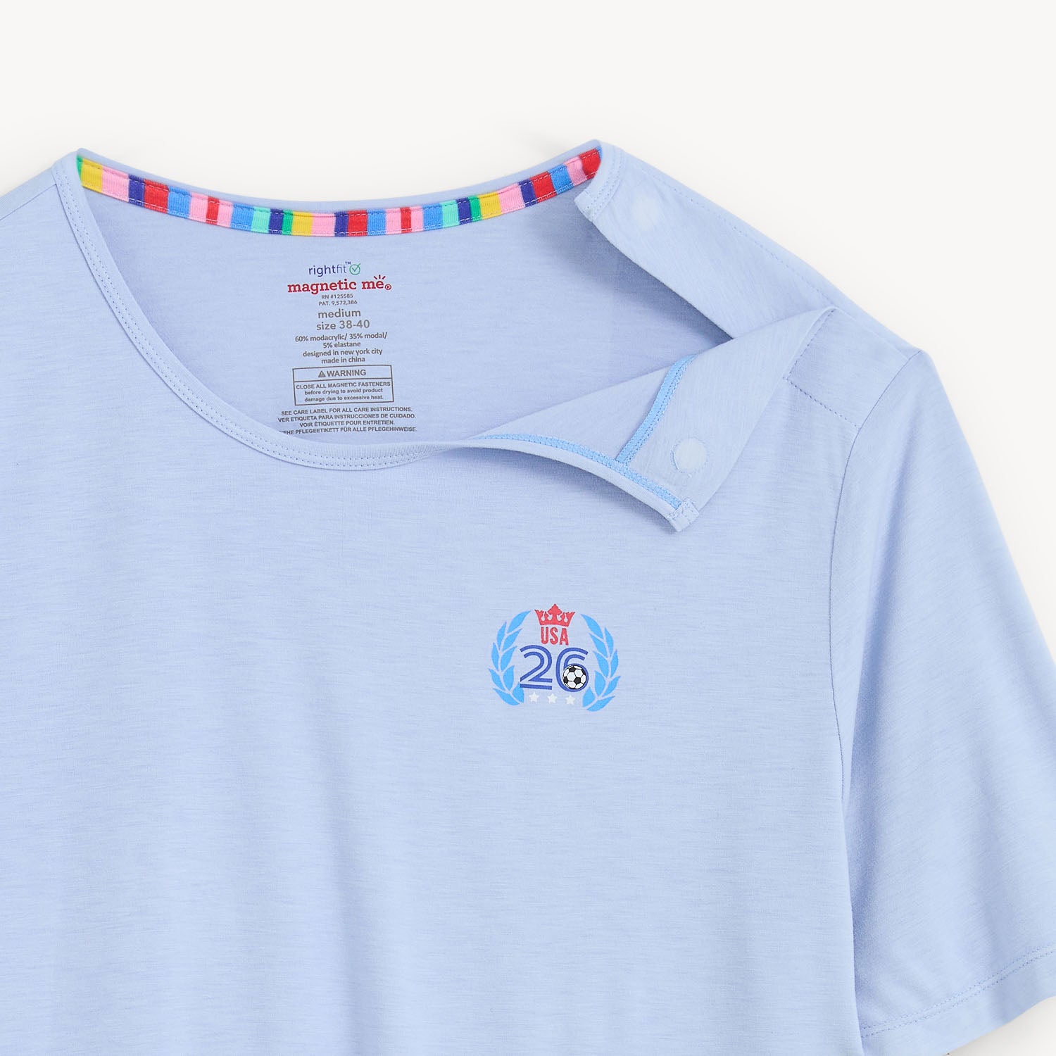 Open magnet on the shoulder side of A men's pajama set featuring a solid light blue short-sleeve t-shirt with a small chest logo and matching white striped jogger pants with an all-over patriotic soccer print, by Magnetic Me.
