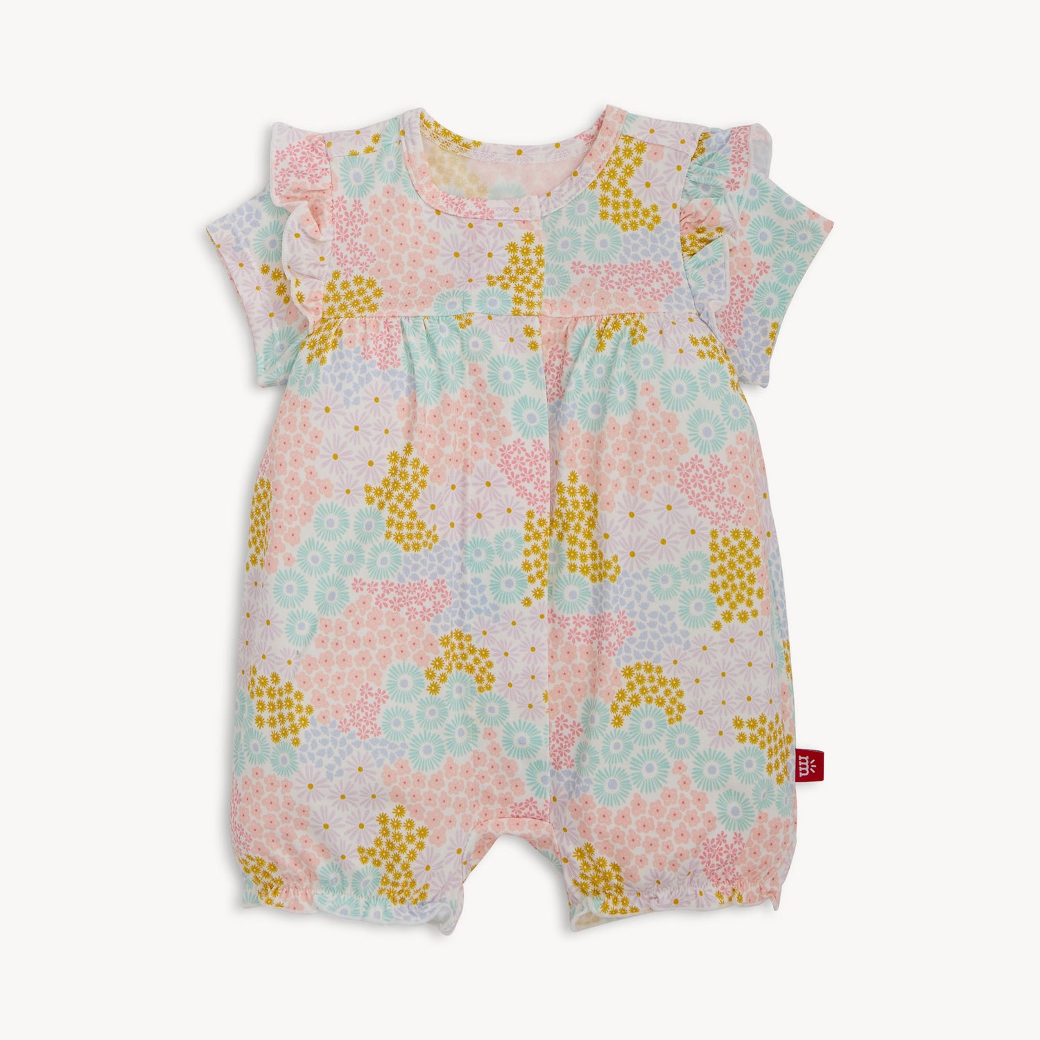 A short-sleeve baby romper with ruffled shoulders and elastic leg openings featuring a dense pastel floral print of pink, yellow, and light blue wildflowers on a white background, by Magnetic Me.