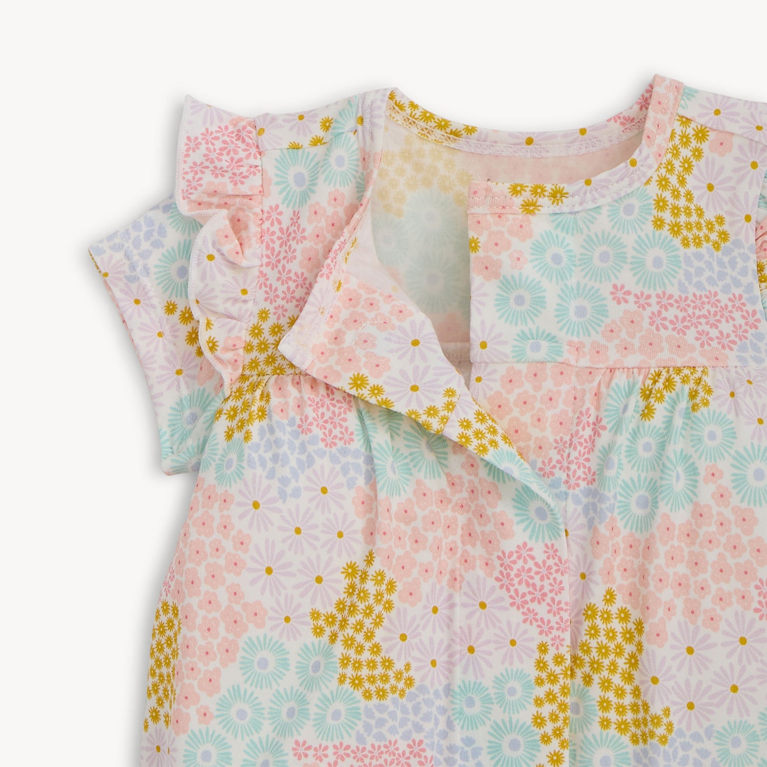 Open magnet in the center front of  A short-sleeve baby romper with ruffled shoulders and elastic leg openings featuring a dense pastel floral print of pink, yellow, and light blue wildflowers on a white background, by Magnetic Me.